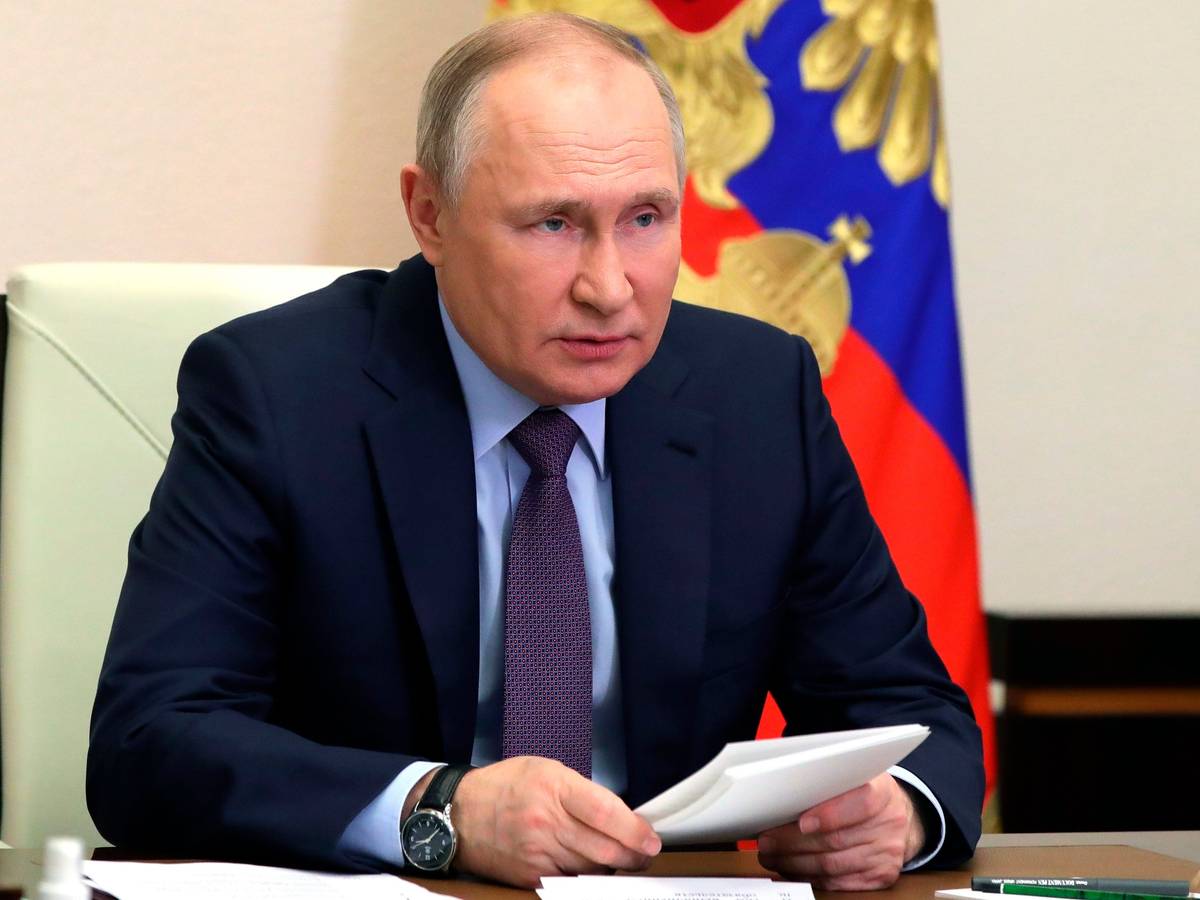 Wladimir Putin sitzt an einem Schreibtisch. Hinter ihm hängt die russische Flagge.