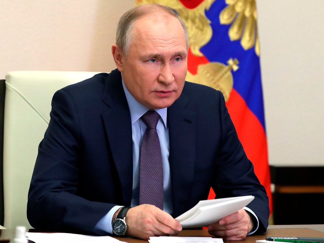 Wladimir Putin sitzt an einem Schreibtisch. Hinter ihm hängt die russische Flagge.