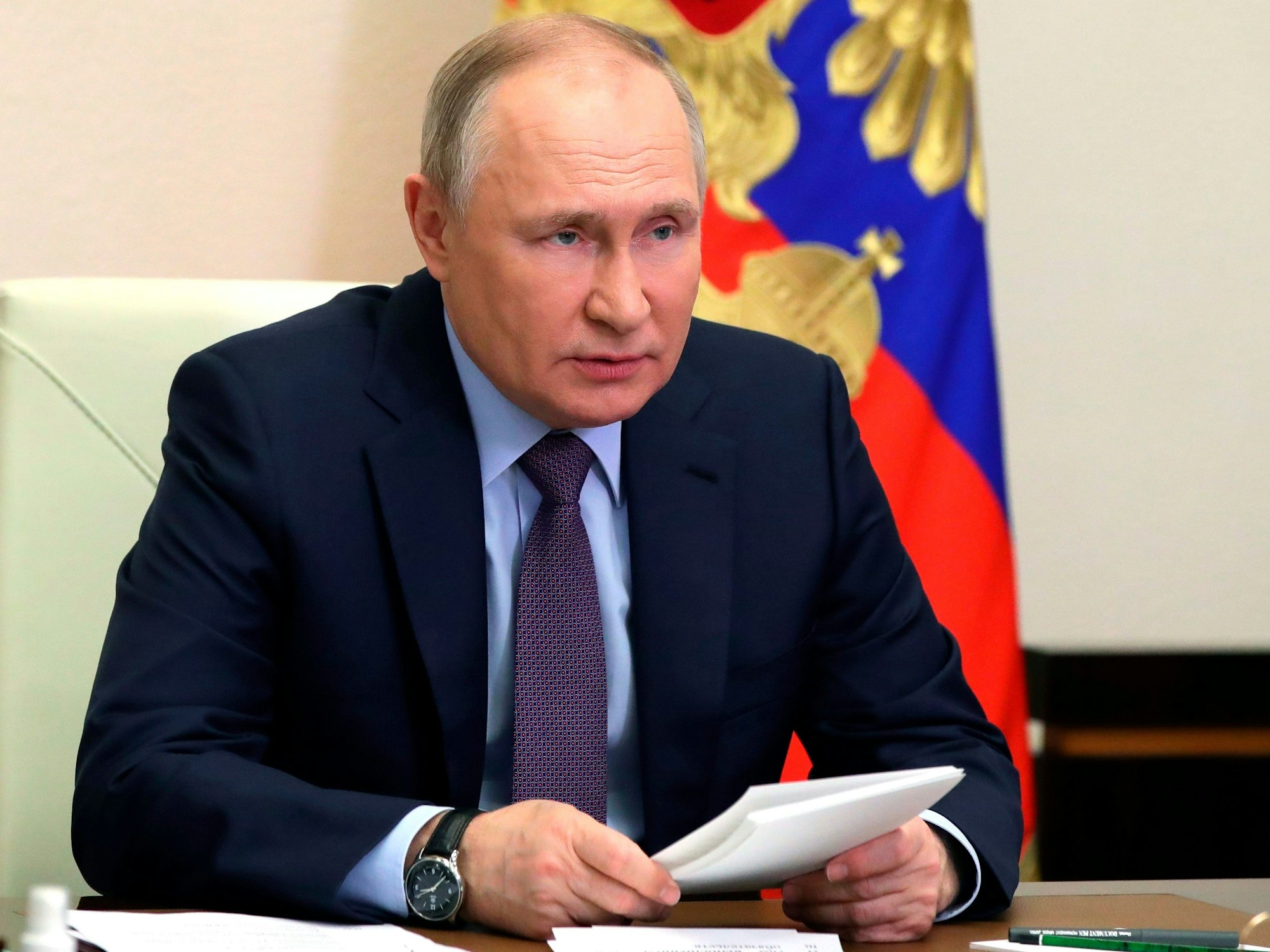 Wladimir Putin sitzt an einem Schreibtisch. Hinter ihm hängt die russische Flagge.
