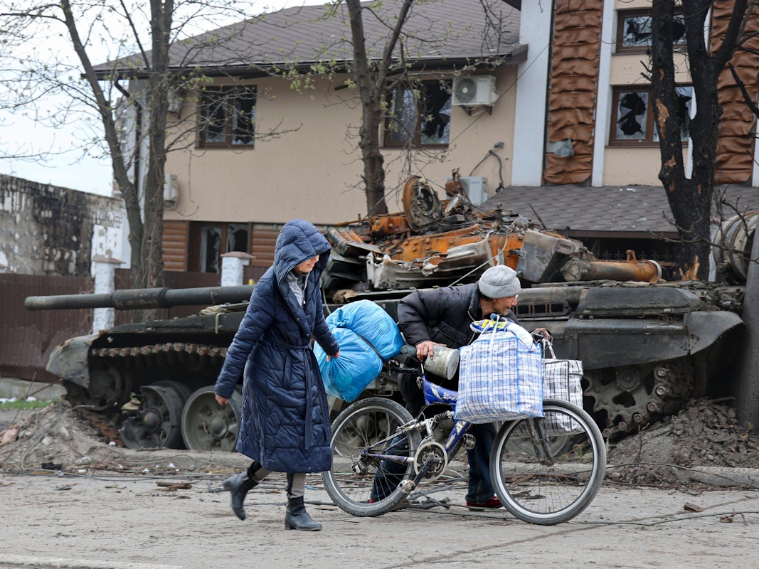 Zwei Personen laufen durch die Kriegstrümmer. Im Hintergrund ist ein zerstörter Panzer zu sehen.