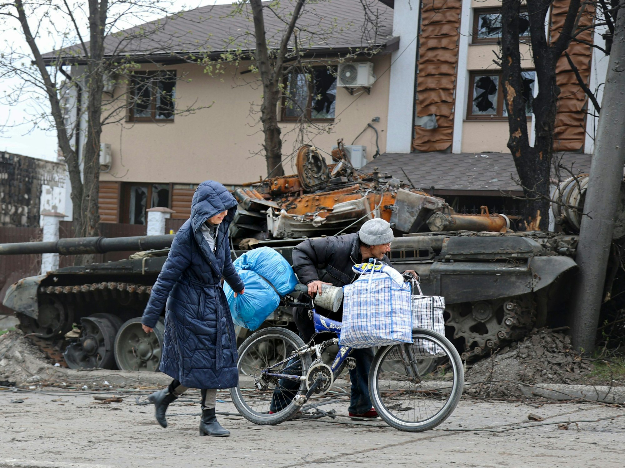 Zwei Personen laufen durch die Kriegstrümmer. Im Hintergrund ist ein zerstörter Panzer zu sehen.