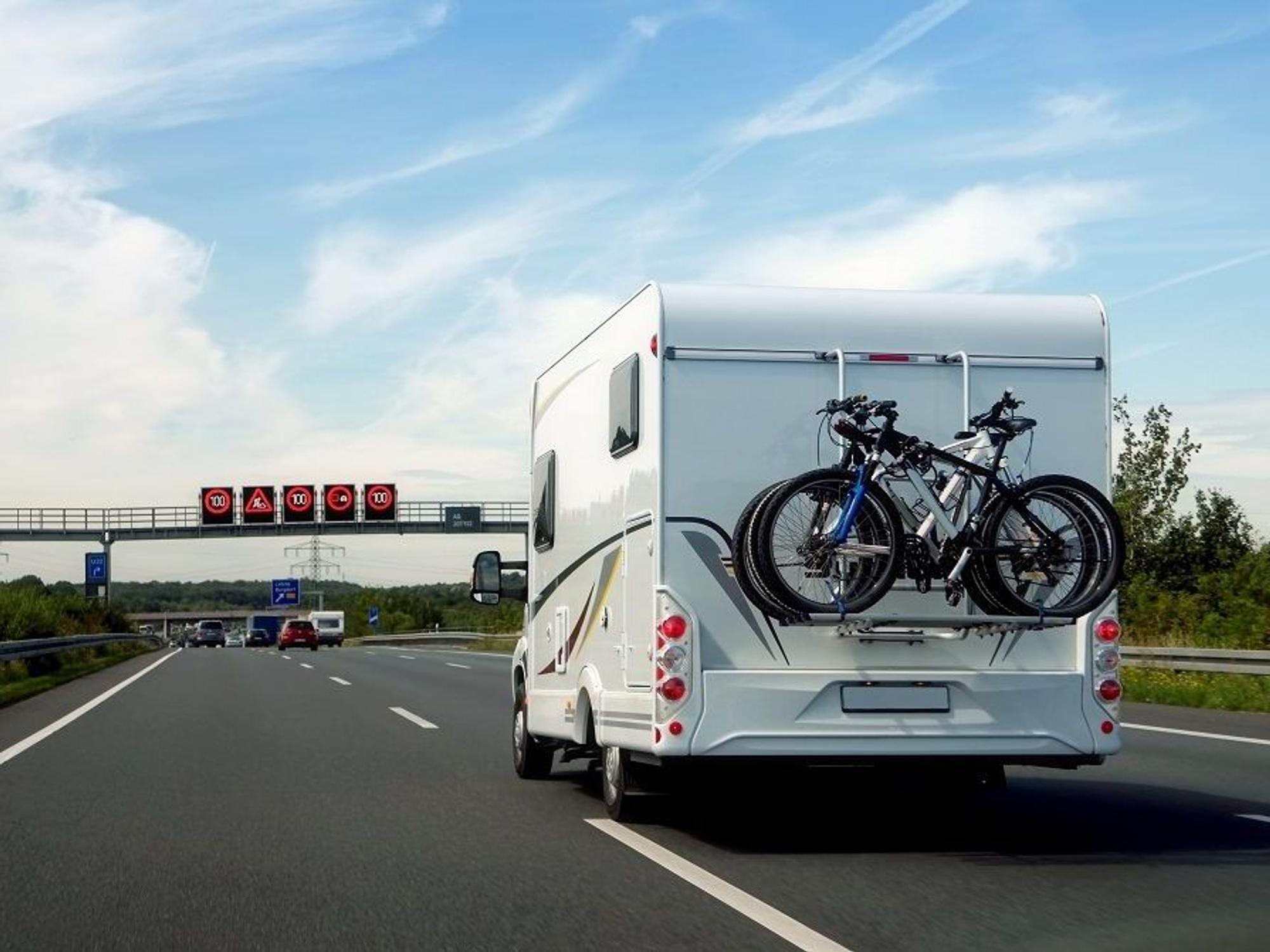 Hier zu sehen: Ein Wohnmobil, auf dem mehrere Fahrräder befestigt sind, fährt auf der Autobahn.