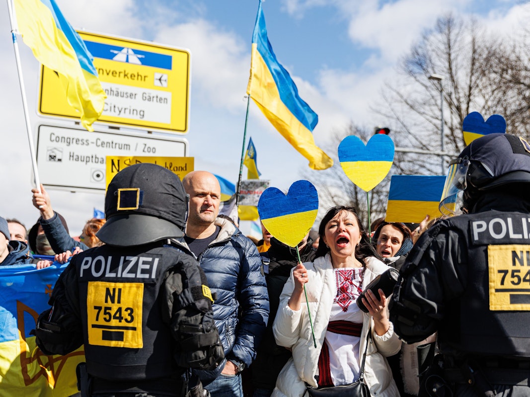 Menschen mit Ukraine-Fahnen werden von Polizisten bewacht.