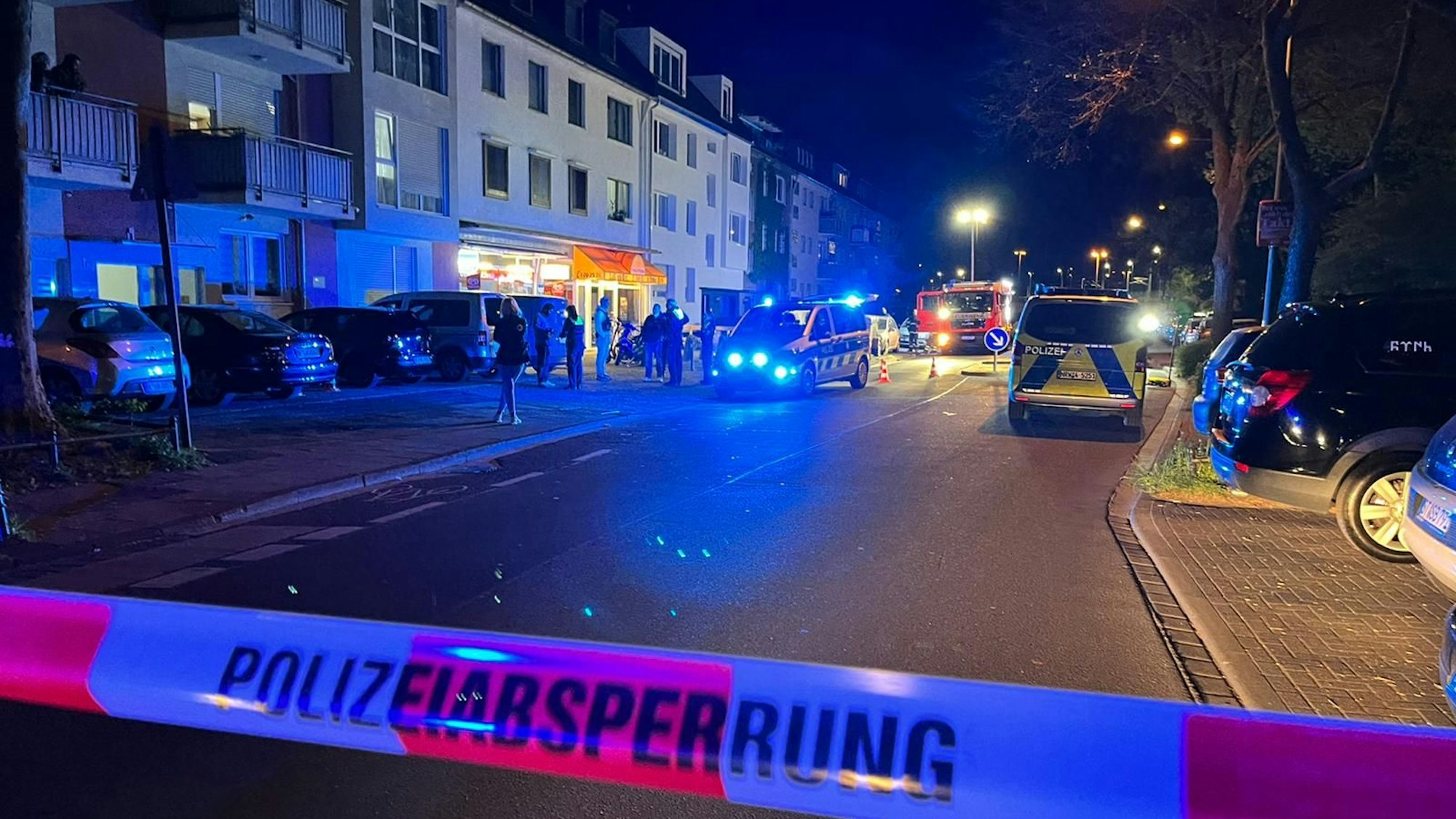 Eine Straße ist mit Flatterband der Polizei abgesperrt. Auf der Straße stehen mehrere Einsatzfahrzeuge vor einem Kiosk.