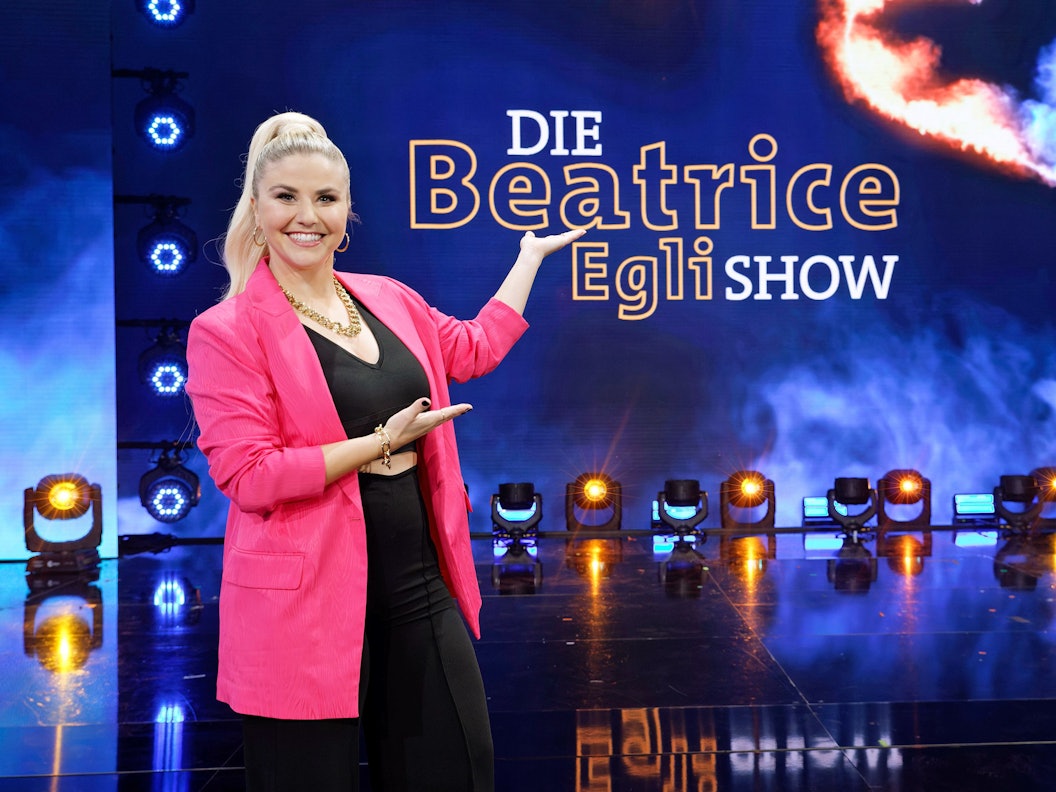 Beatrice Egli zeigt auf das neue Logo ihrer Schlagershow „Die Beatrice Egli Show“.