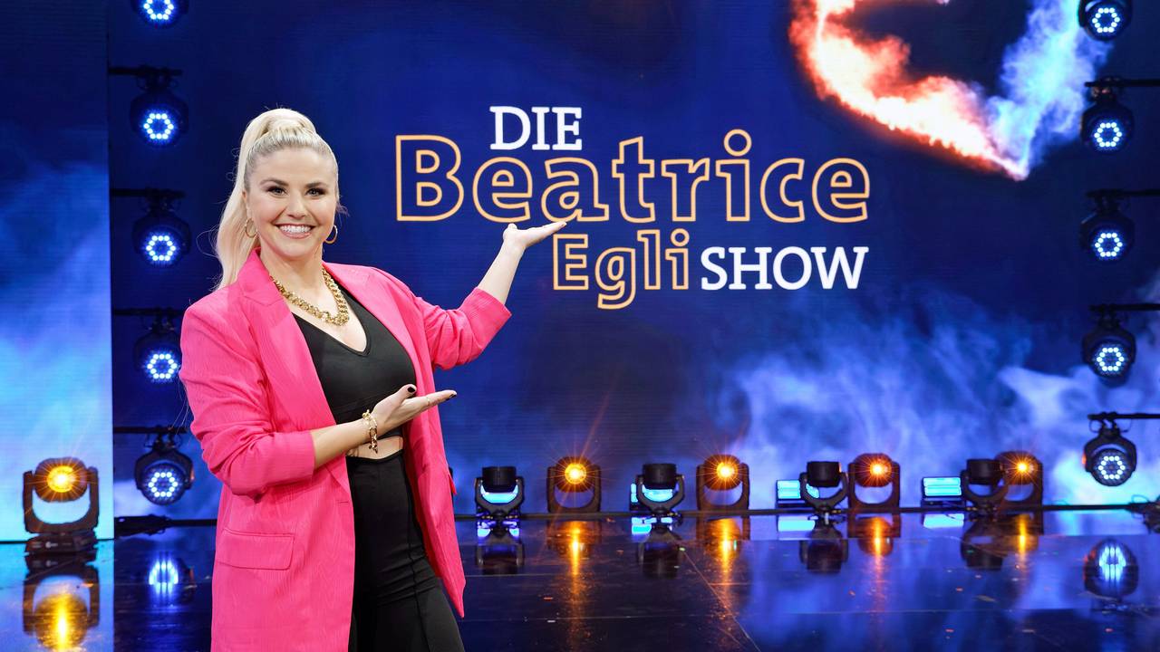 Beatrice Egli zeigt auf das neue Logo ihrer Schlagershow „Die Beatrice Egli Show“.