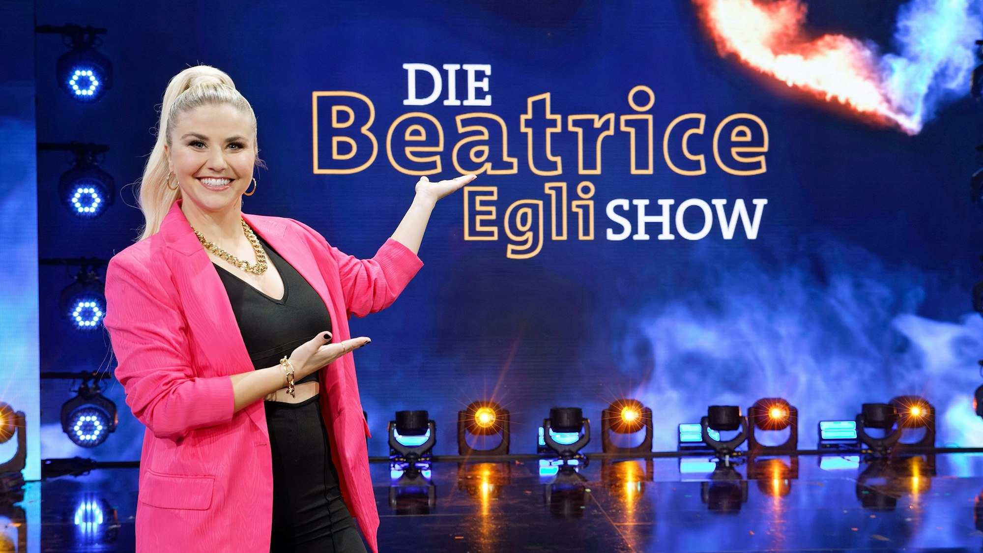 Beatrice Egli zeigt auf das neue Logo ihrer Schlagershow „Die Beatrice Egli Show“.