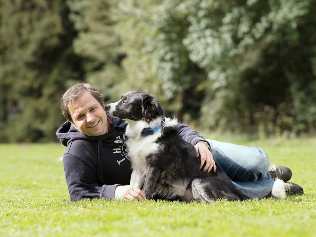 Martin Rütter liegt neben einem Hund auf einer Wiese.