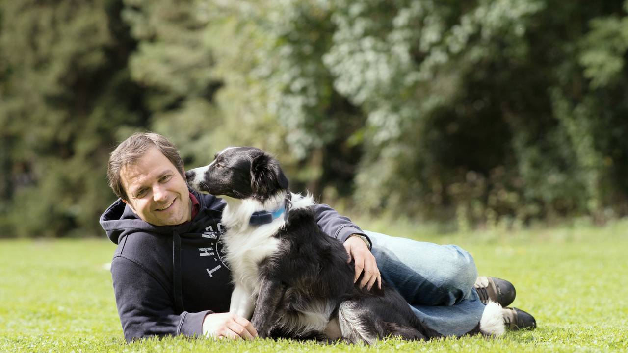 Martin Rütter liegt neben einem Hund auf einer Wiese.