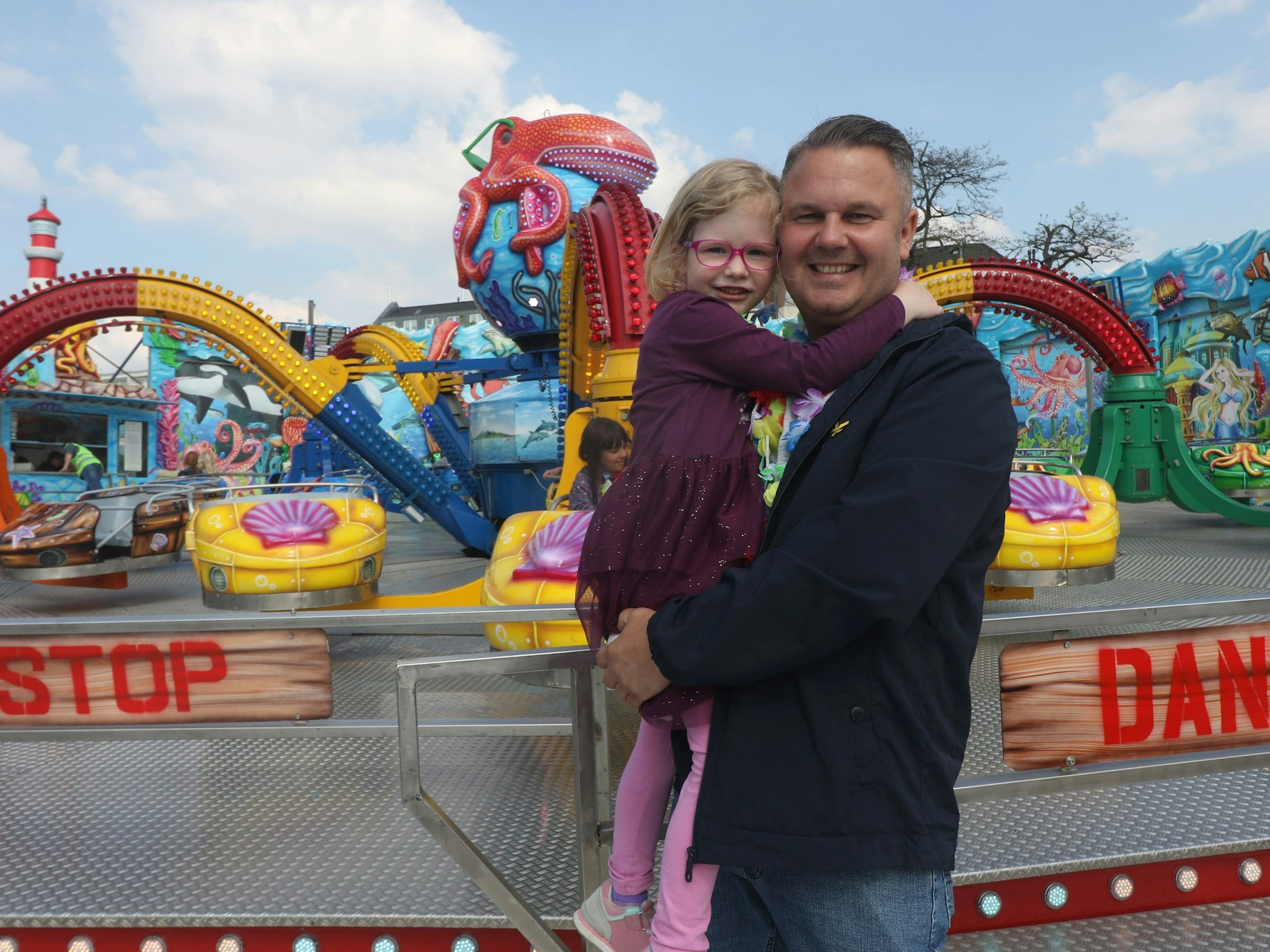 Ein Mann steht mit seinem Kind vor einem Fahrgeschäft auf der Deutzer Kirmes.