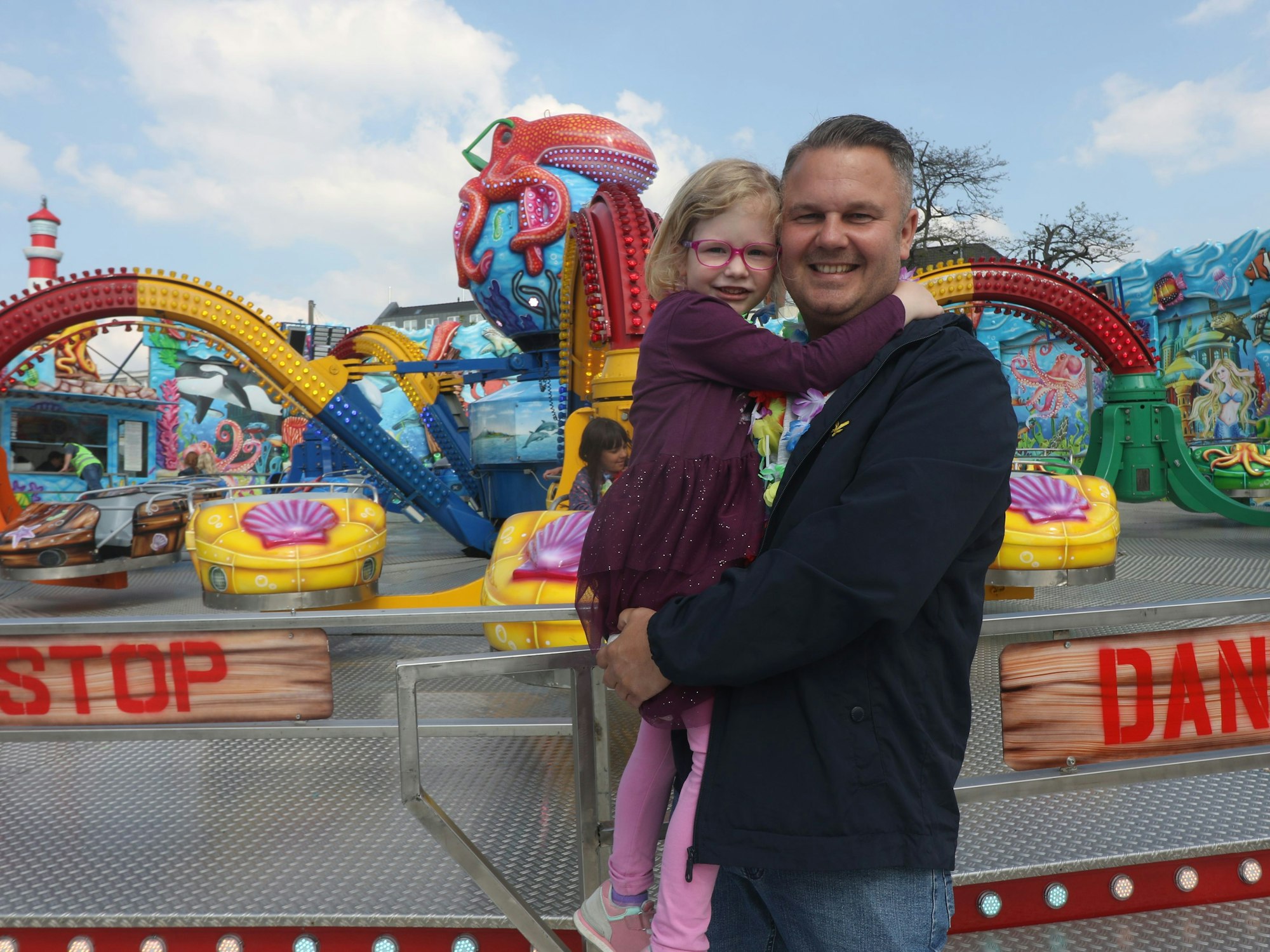Ein Mann steht mit seinem Kind vor einem Fahrgeschäft auf der Deutzer Kirmes.