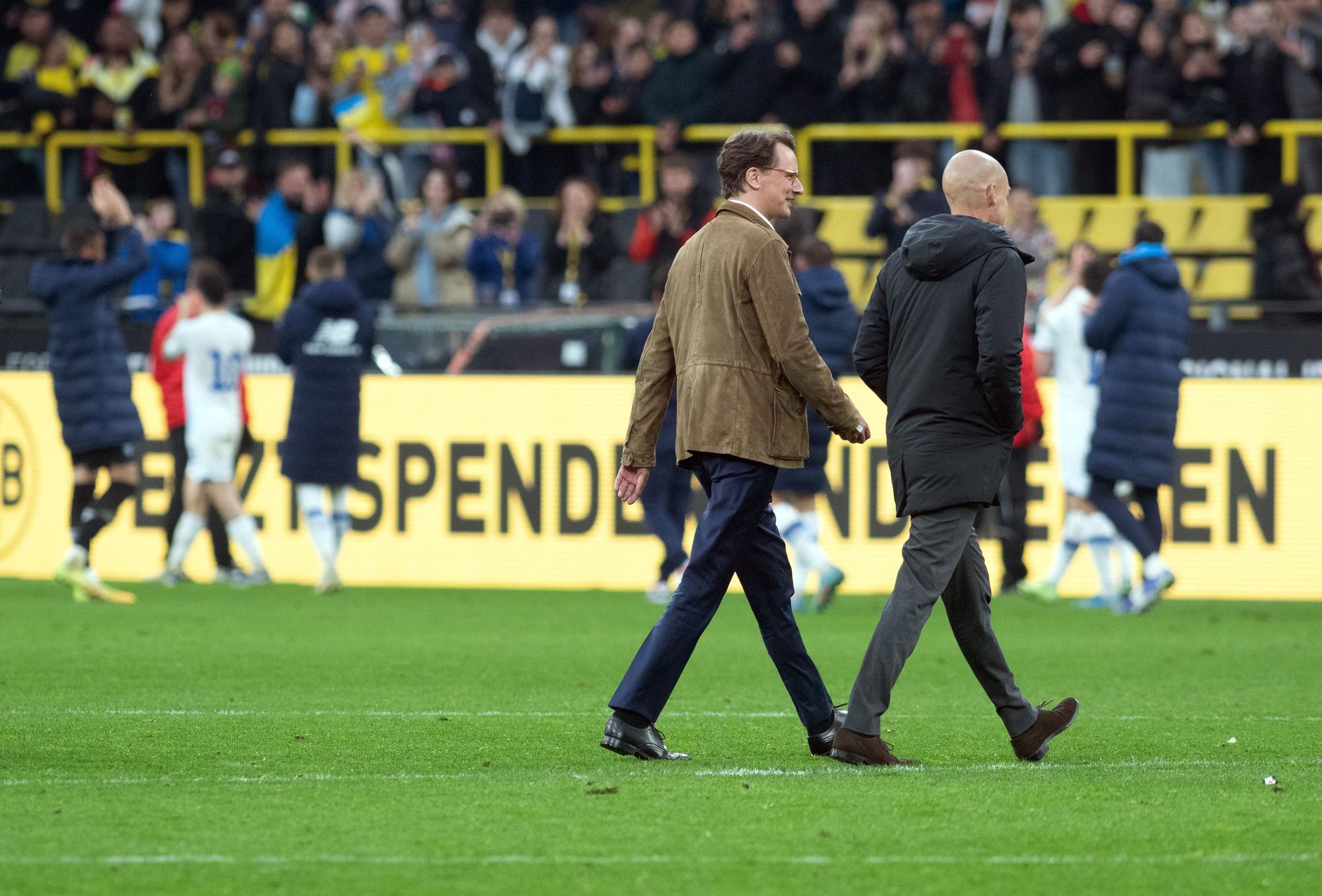 Hendrik Wüst geht mit BVB-Marketingchef Carsten Cramer über den Rasen im Stadion.
