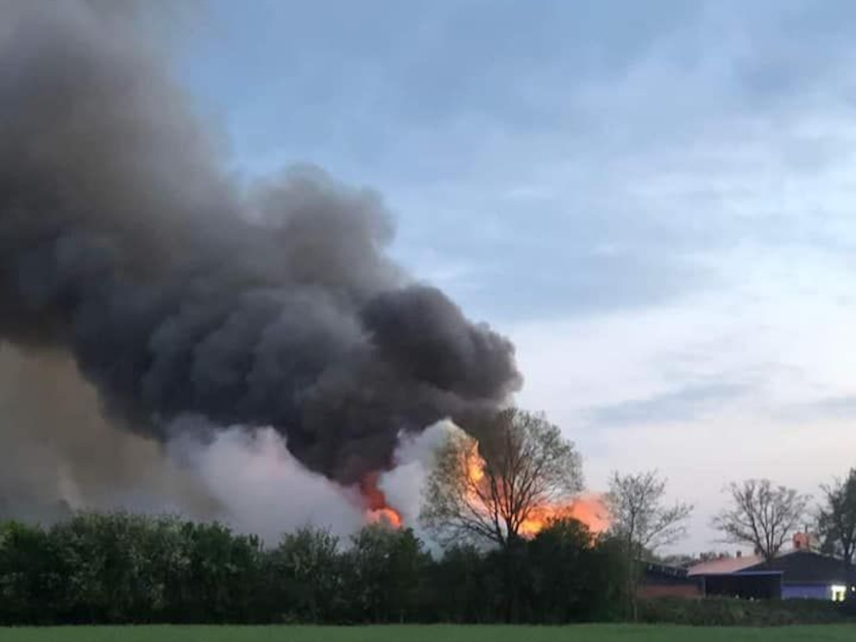 Von weitem sieht man hinter Bäumen lodernde Flammen und eine enorme Rauchsäule.