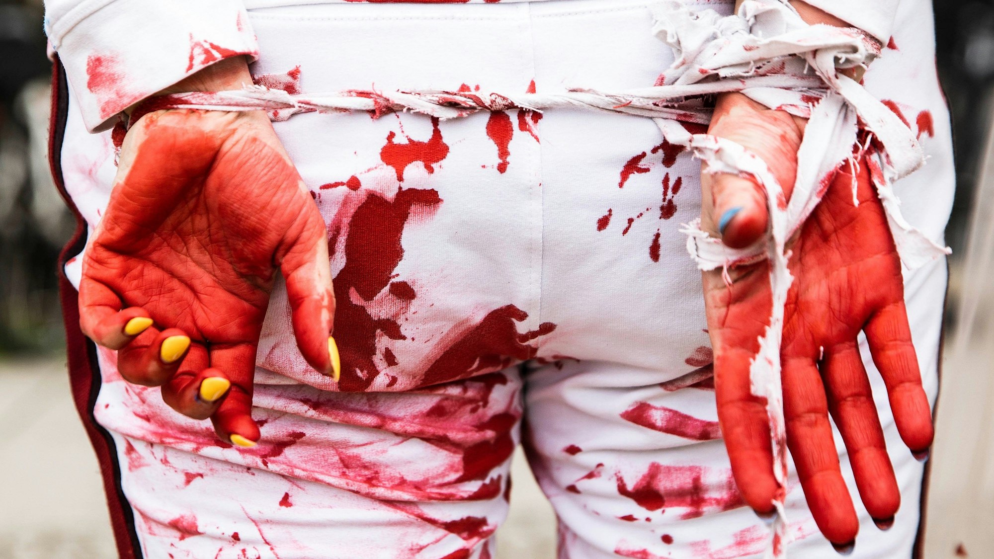 Eine Teilnehmerin protestiert mit zusammengebundenen Händen gemeinsam mit anderen Frauen in weißer Kleidung mit künstlichem Blut darauf sowie verbundenen Händen bei einer Demonstration gegen die Gewalt an Frauen und Mädchen beim russischen Angriffskrieg auf die Ukraine.