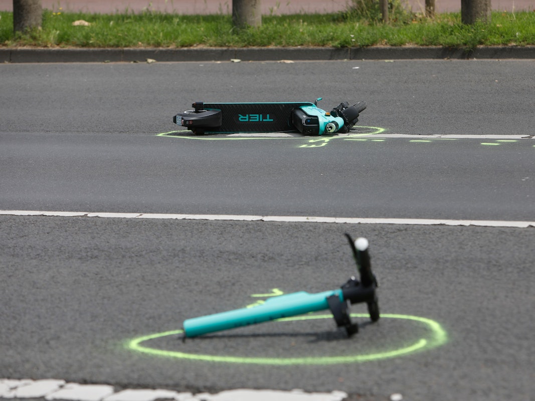 Zwei Teile eines verunfallten E-Scooters liegen auf der Rheinuferstraße in Köln.