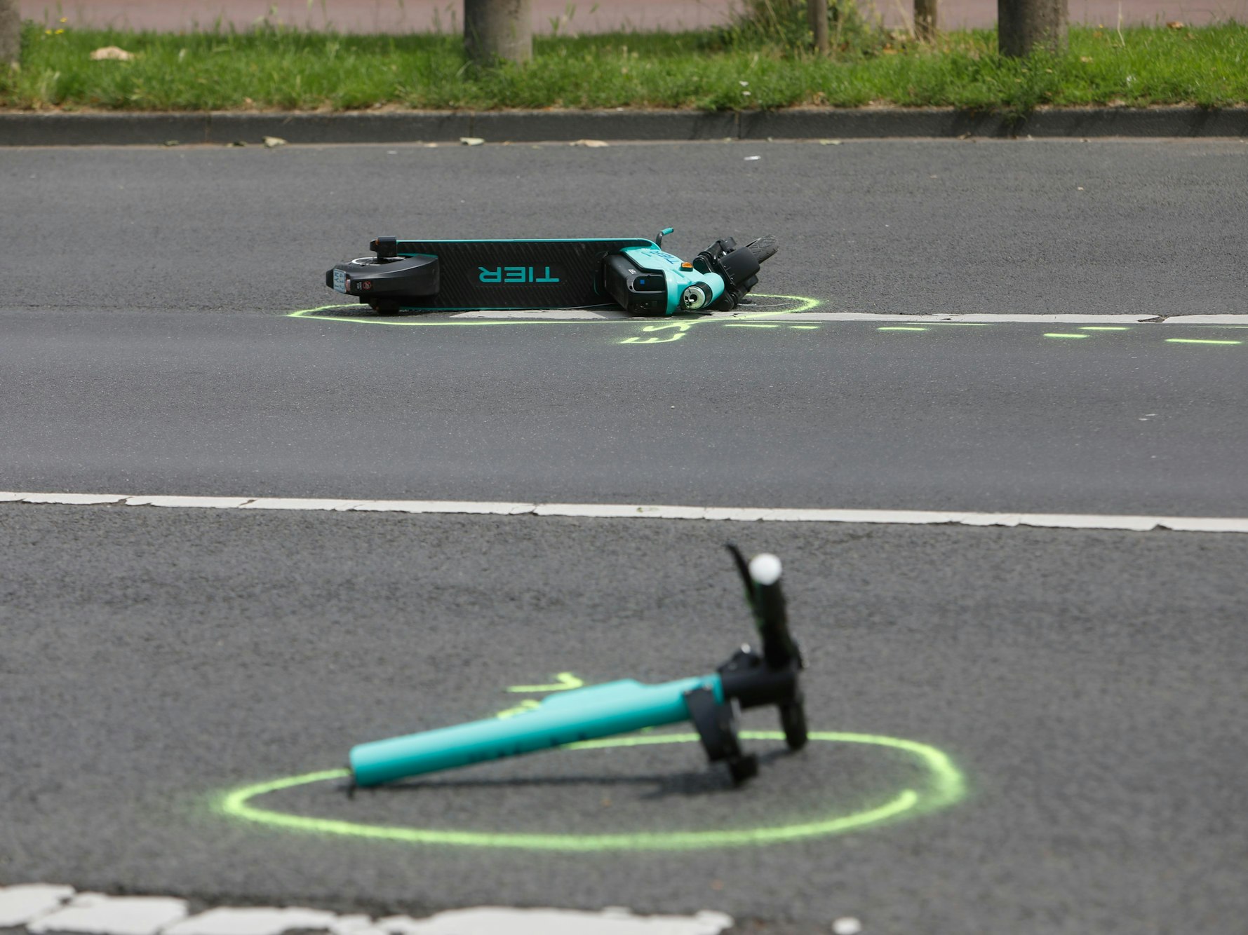 Zwei Teile eines verunfallten E-Scooters liegen auf der Rheinuferstraße in Köln.