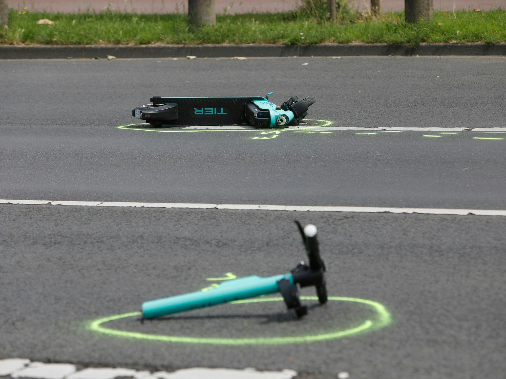 Zwei Teile eines verunfallten E-Scooters liegen auf der Rheinuferstraße in Köln.