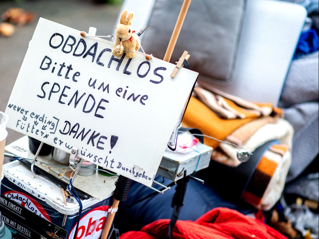 Ein Schild mit der Aufschrift „Obdachlos - bitte um eine Spende - danke!“ steht neben den Habseligkeiten eines Obdachlosen, die auf einem Bürgersteig in der Innenstadt liegen.