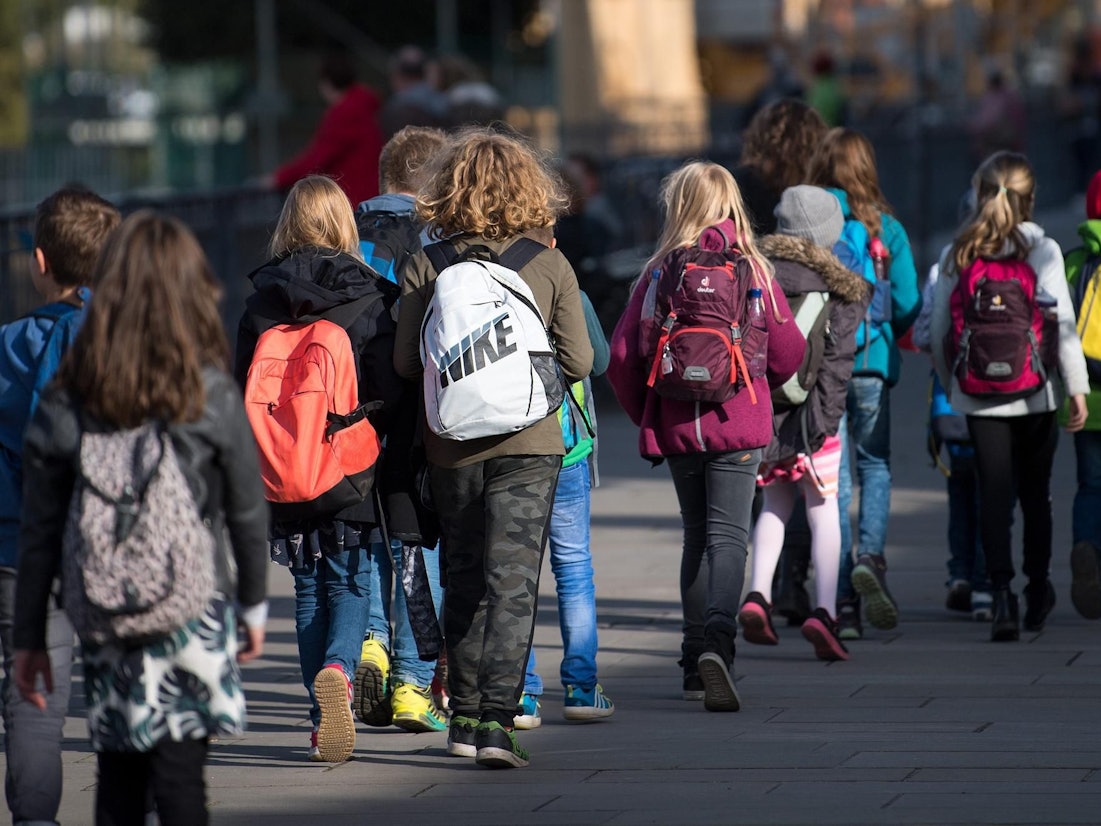 Schulkinder mit Rucksäcken gehen auf einer Straße.