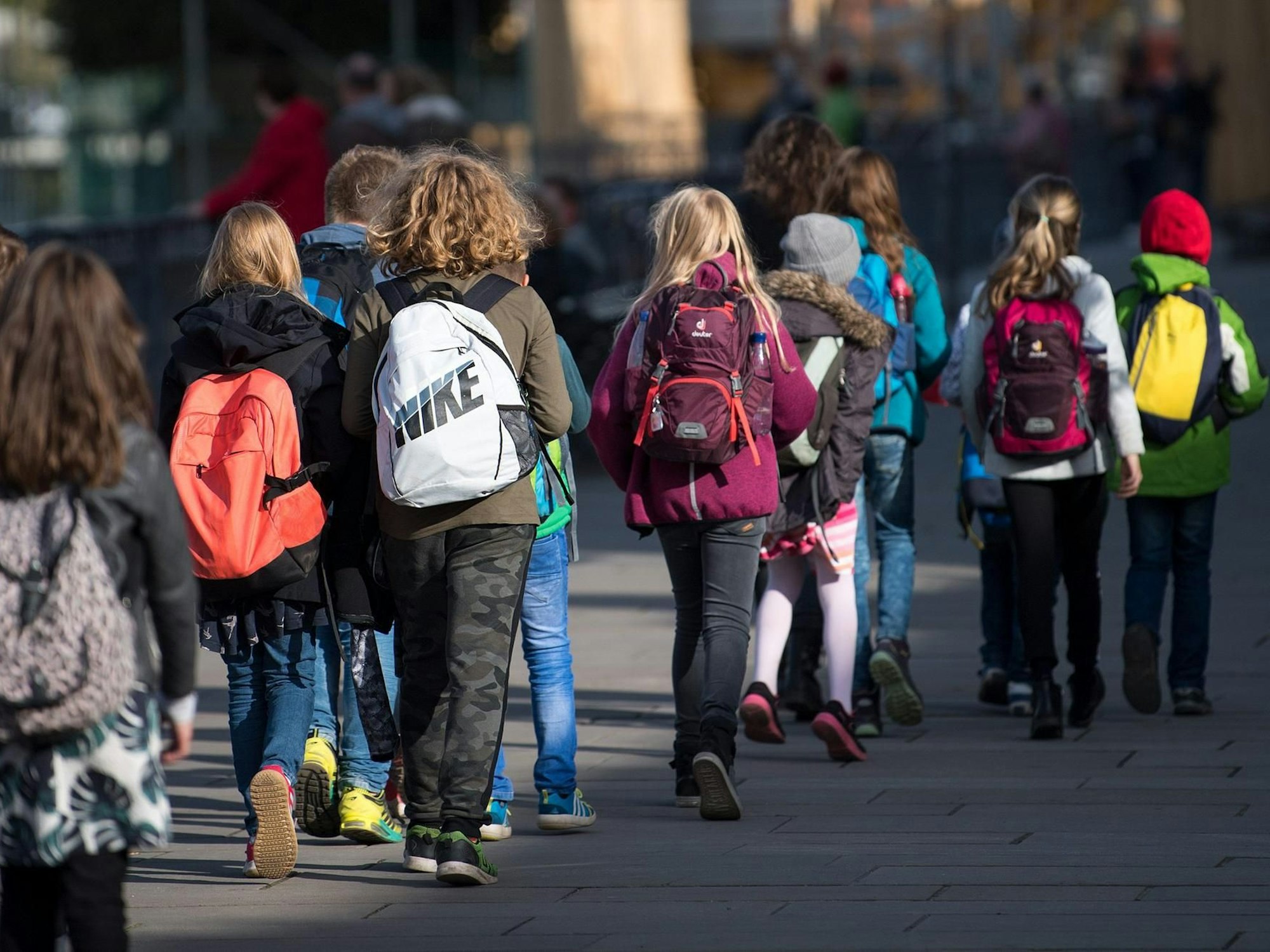 Schulkinder mit Rucksäcken gehen auf einer Straße.