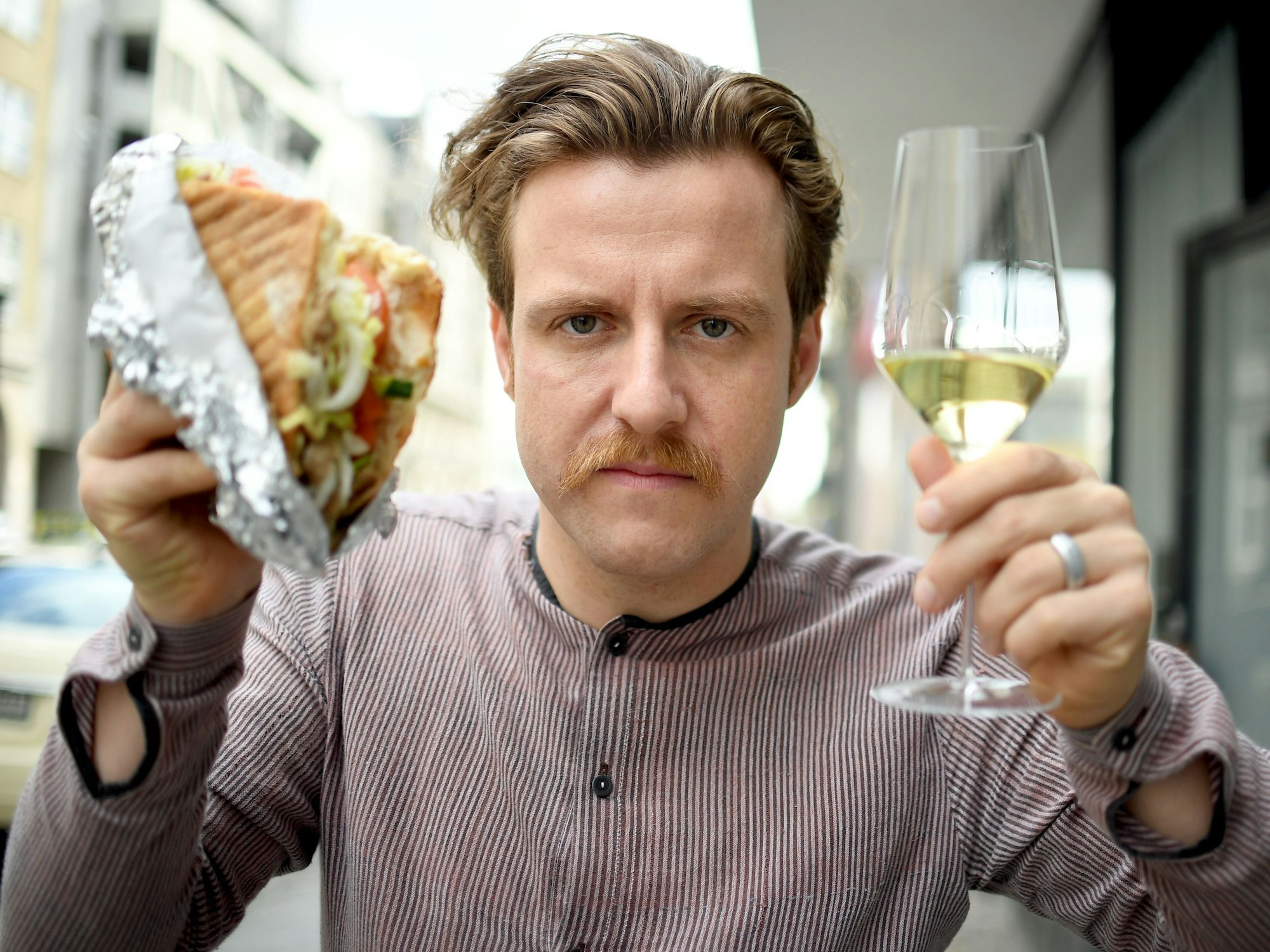 Sommelier Billy Wagner hält am 13.10.2017 in Berlin einen Döner und ein Glas Wein in der Hand.