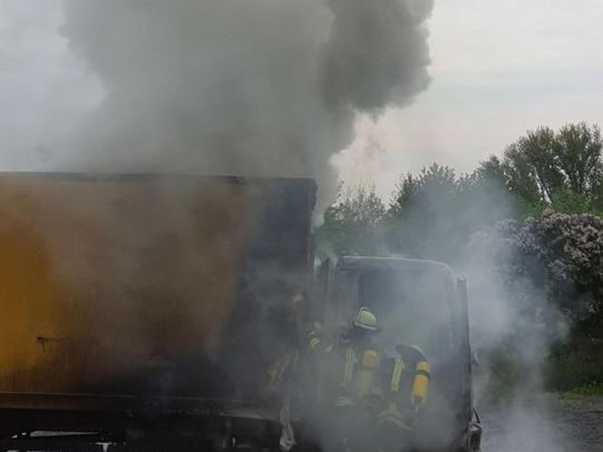 Ein Lkw brennt, es kommt zu starker Rauchentwicklung, zwei Feuerwehrmänner löschen unter Atemschutz.