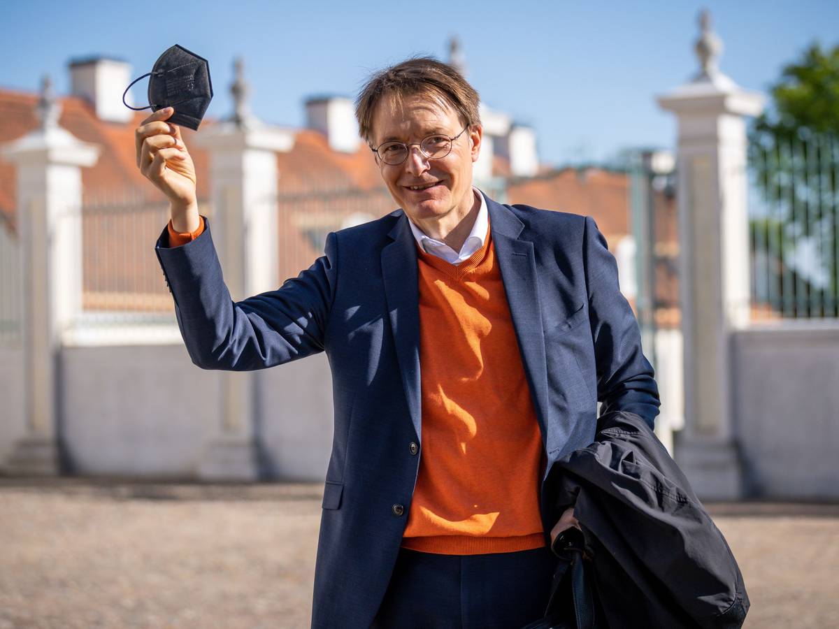 Der Bundesgesundheitsminister Karl Lauterbach (SPD) lächelnd mit erhobener Hand und einer Maske in der Hand am 3. Mai 2022 in Brandenburg.