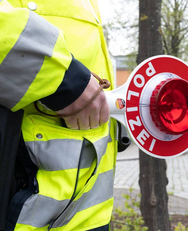 Ein Polizist steht mit einer Winkerkelle an einer Straße vor einem PKW.