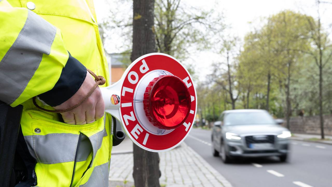 Ein Polizist steht mit einer Winkerkelle an einer Straße vor einem PKW.