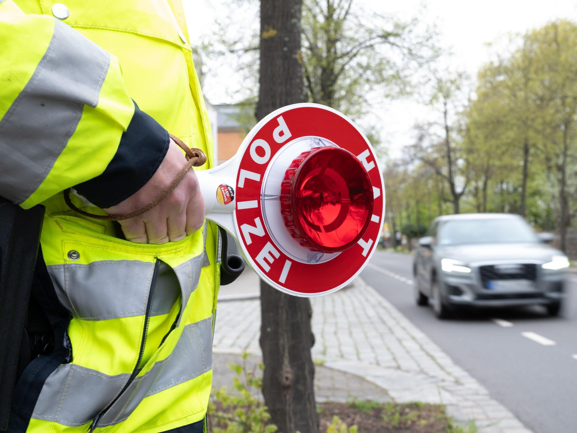 Ein Polizist steht mit einer Winkerkelle an einer Straße vor einem PKW.