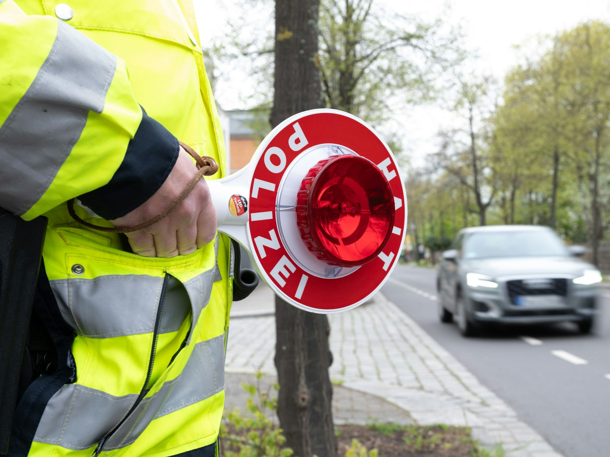 Ein Polizist steht mit einer Winkerkelle an einer Straße vor einem PKW.