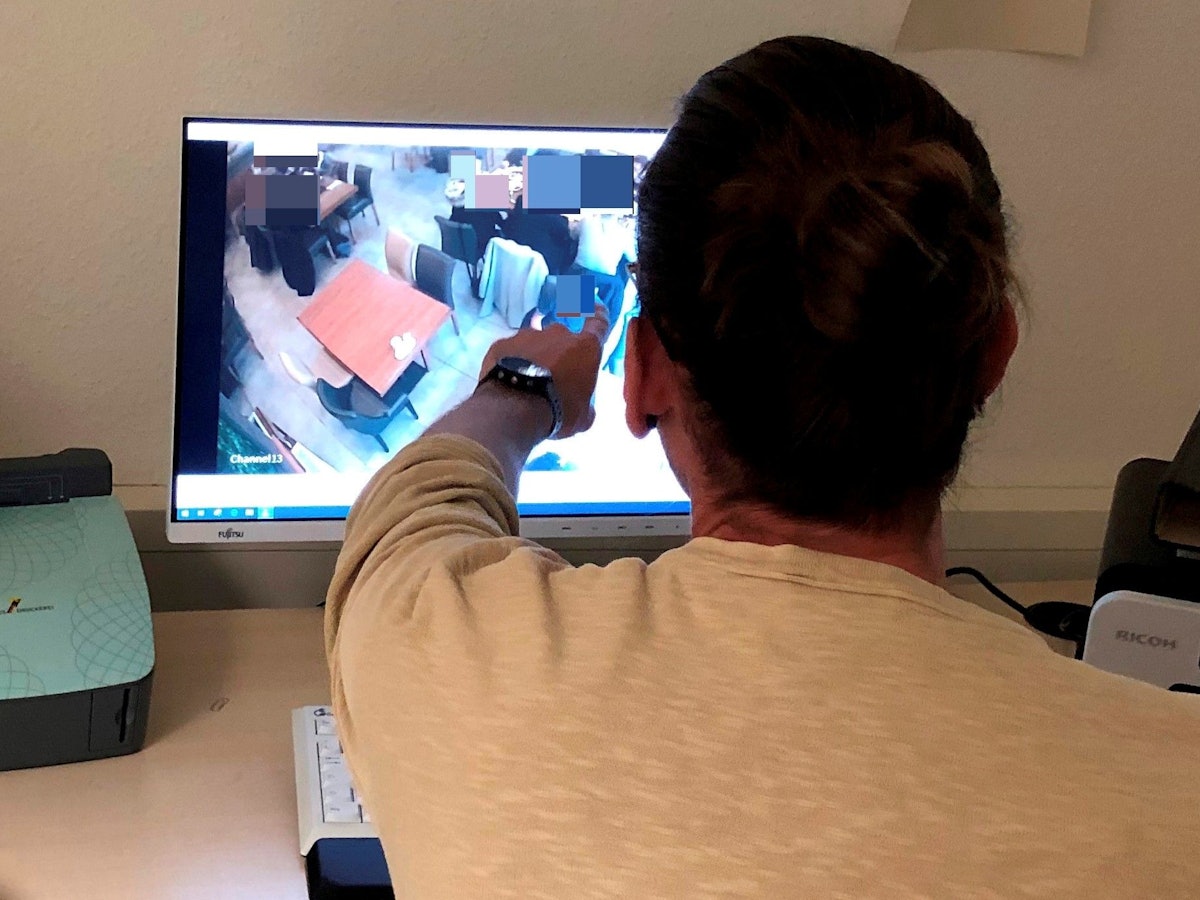 Polizist Niklas B. (39, Name geändert) sitzt vor einem Computerbildschirm und zeigt auf eine Person, die dort auf einem Überwachungsbild zu sehen ist.