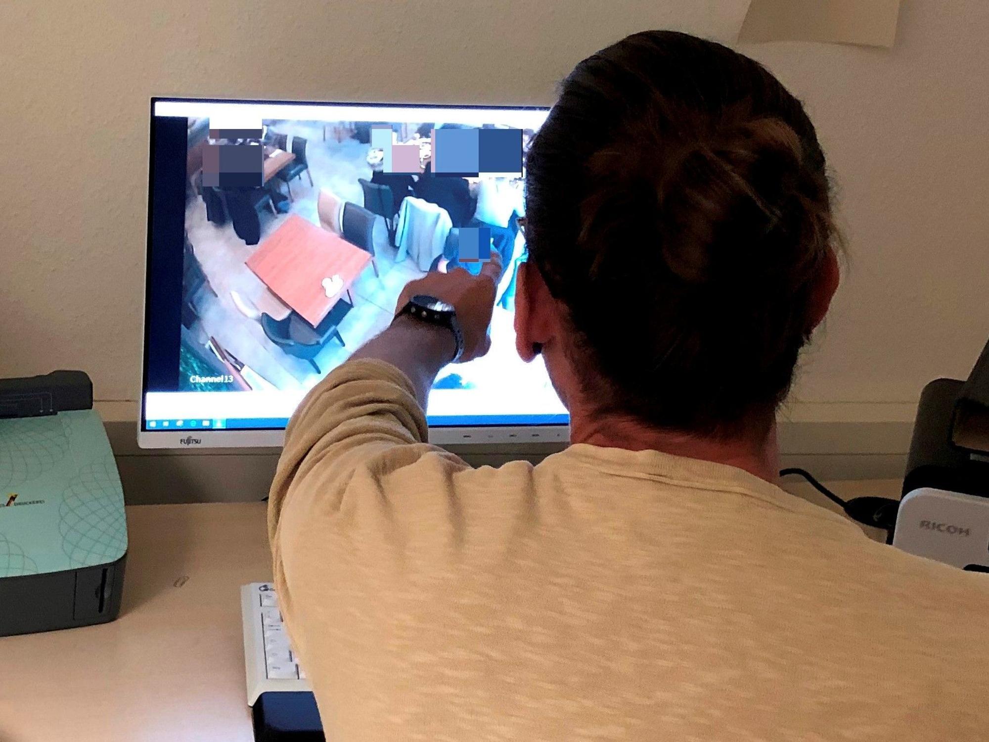 Polizist Niklas B. (39, Name geändert) sitzt vor einem Computerbildschirm und zeigt auf eine Person, die dort auf einem Überwachungsbild zu sehen ist.