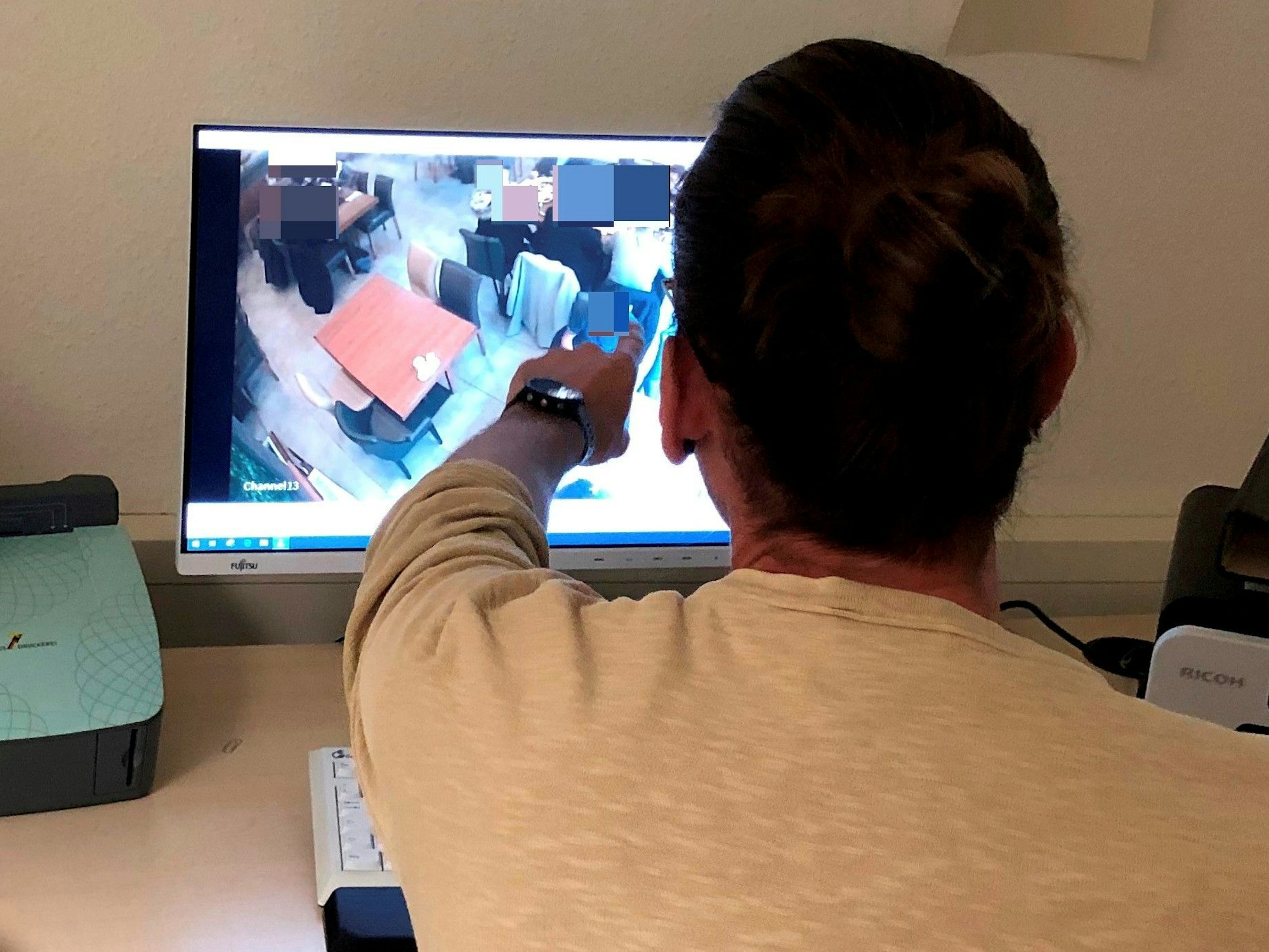 Polizist Niklas B. (39, Name geändert) sitzt vor einem Computerbildschirm und zeigt auf eine Person, die dort auf einem Überwachungsbild zu sehen ist.