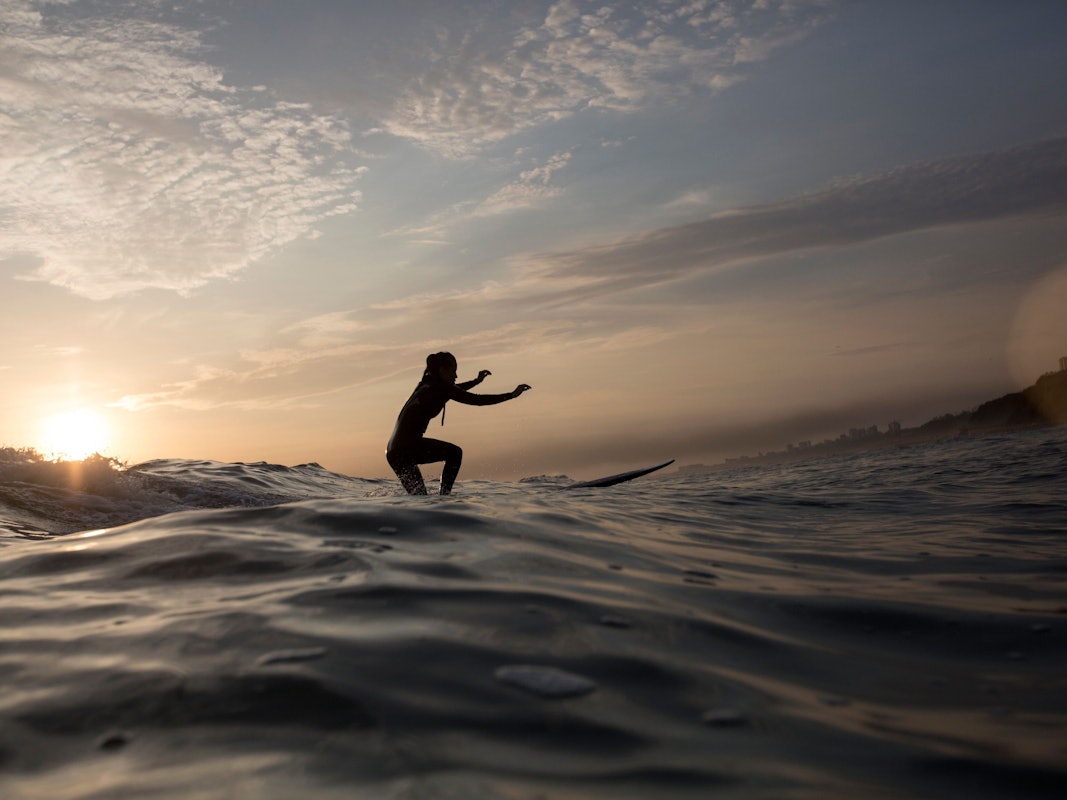 Eine Frau surft bei Sonnenuntergang.