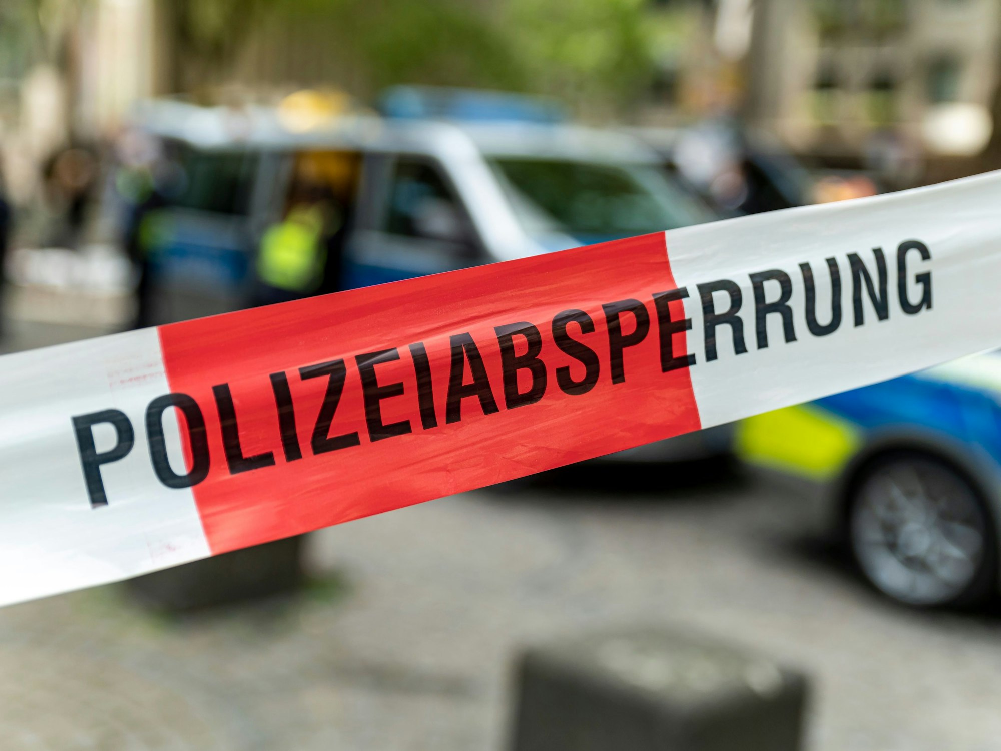 Hinter einer Polizeiabsperrung sind Polizeifahrzeuge zu sehen.