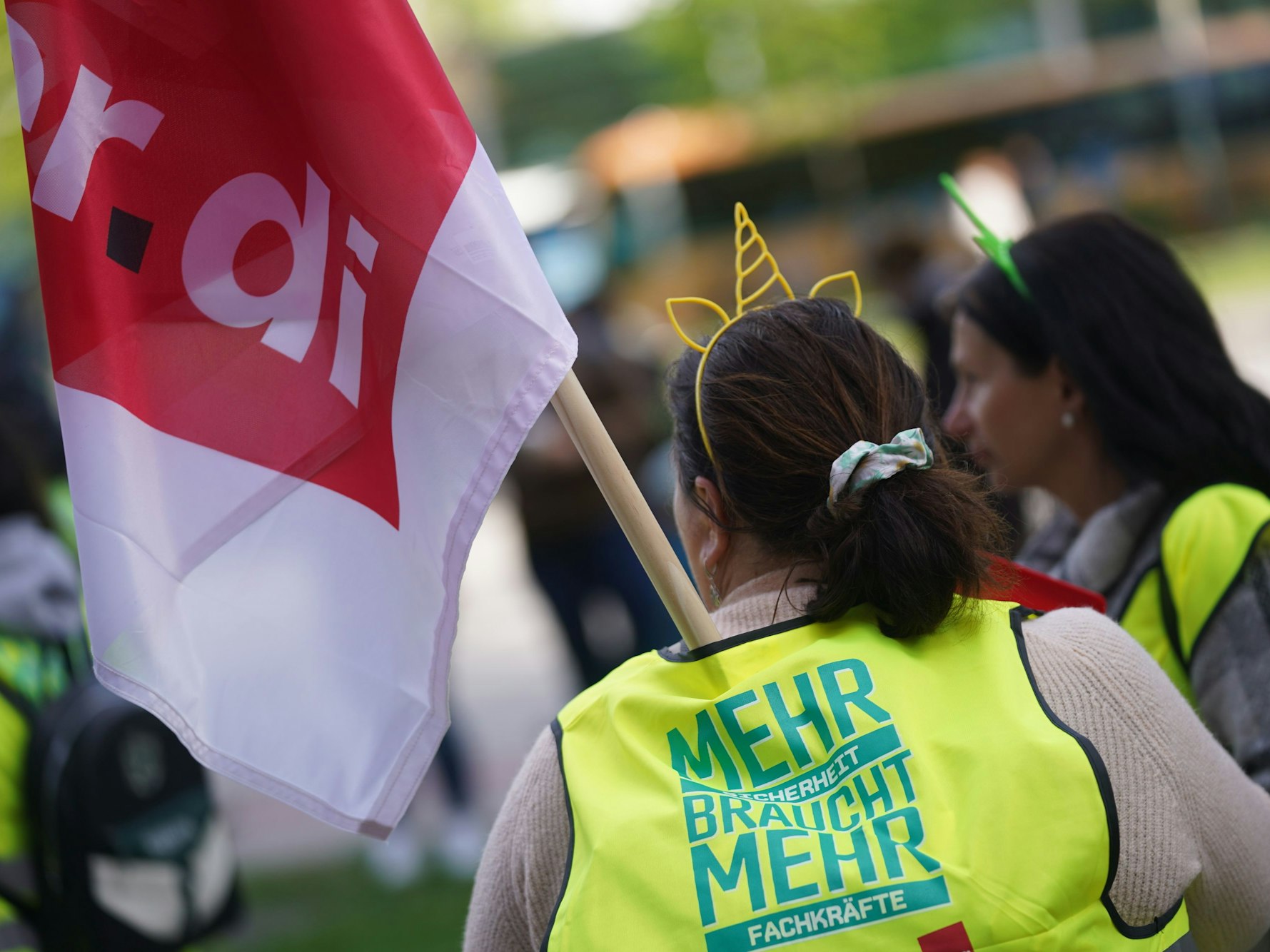 Eine Frau mit Warnweste hält eine Fahne der Gewerkschaft verdi in die Höhe.