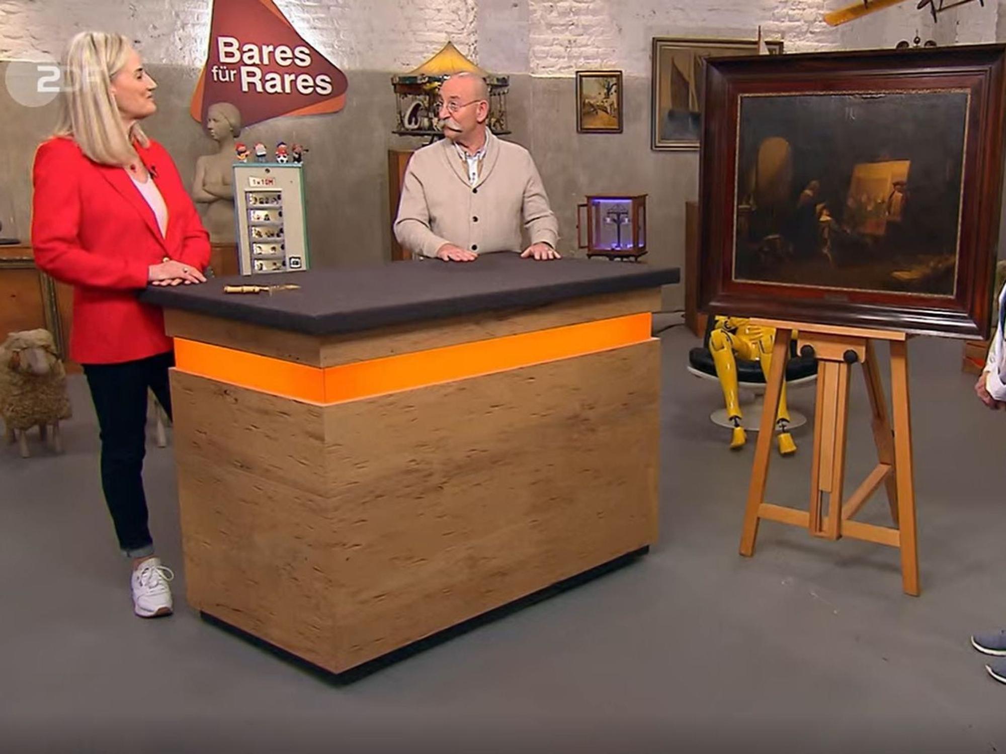 „Bares für Rares“-Expertin Friederike Werner (l.) und Horst Lichter (r.) stehen am Pult und bestaunen ein Gemälde.
