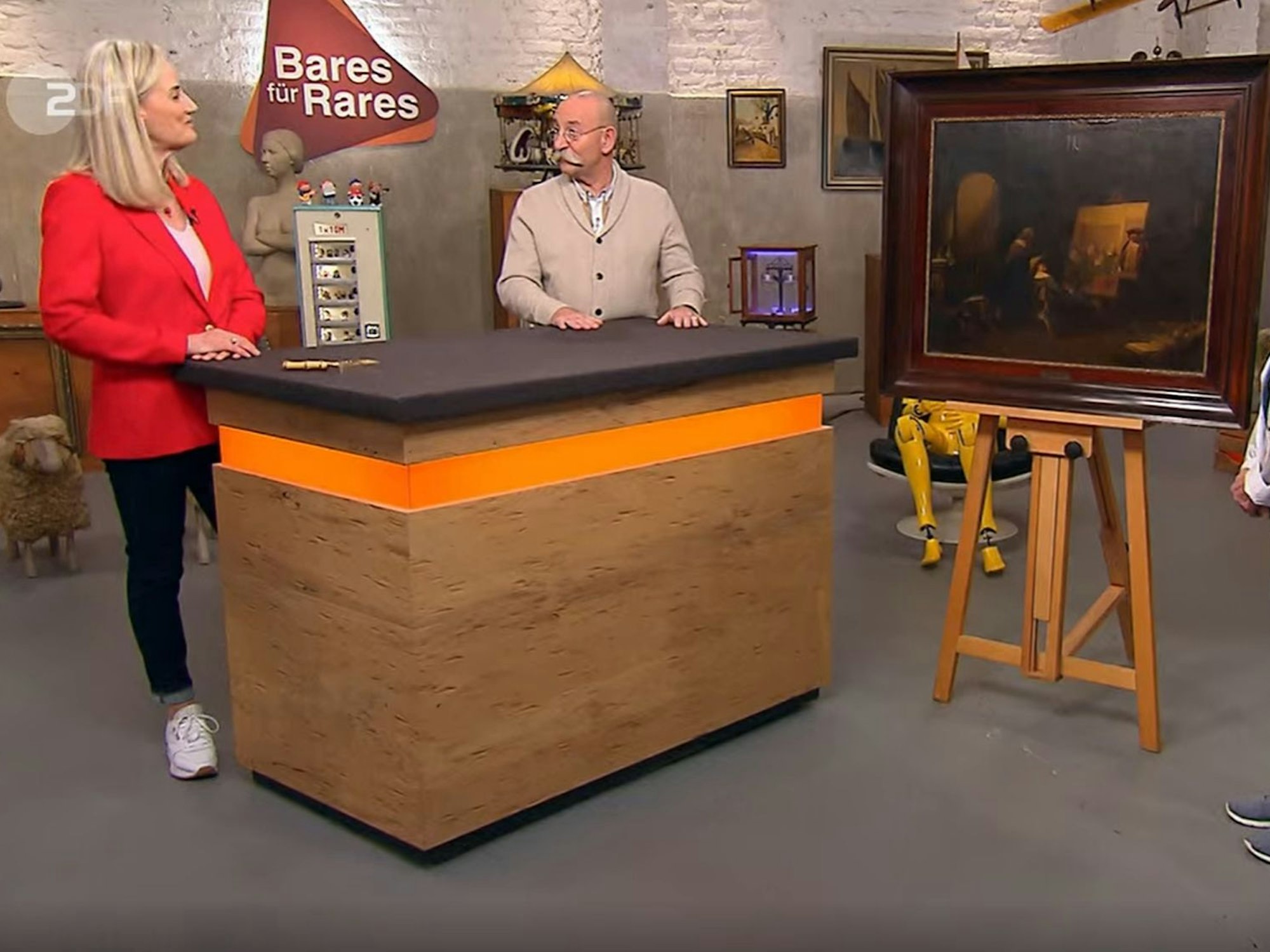 „Bares für Rares“-Expertin Friederike Werner (l.) und Horst Lichter (r.) stehen am Pult und bestaunen ein Gemälde.