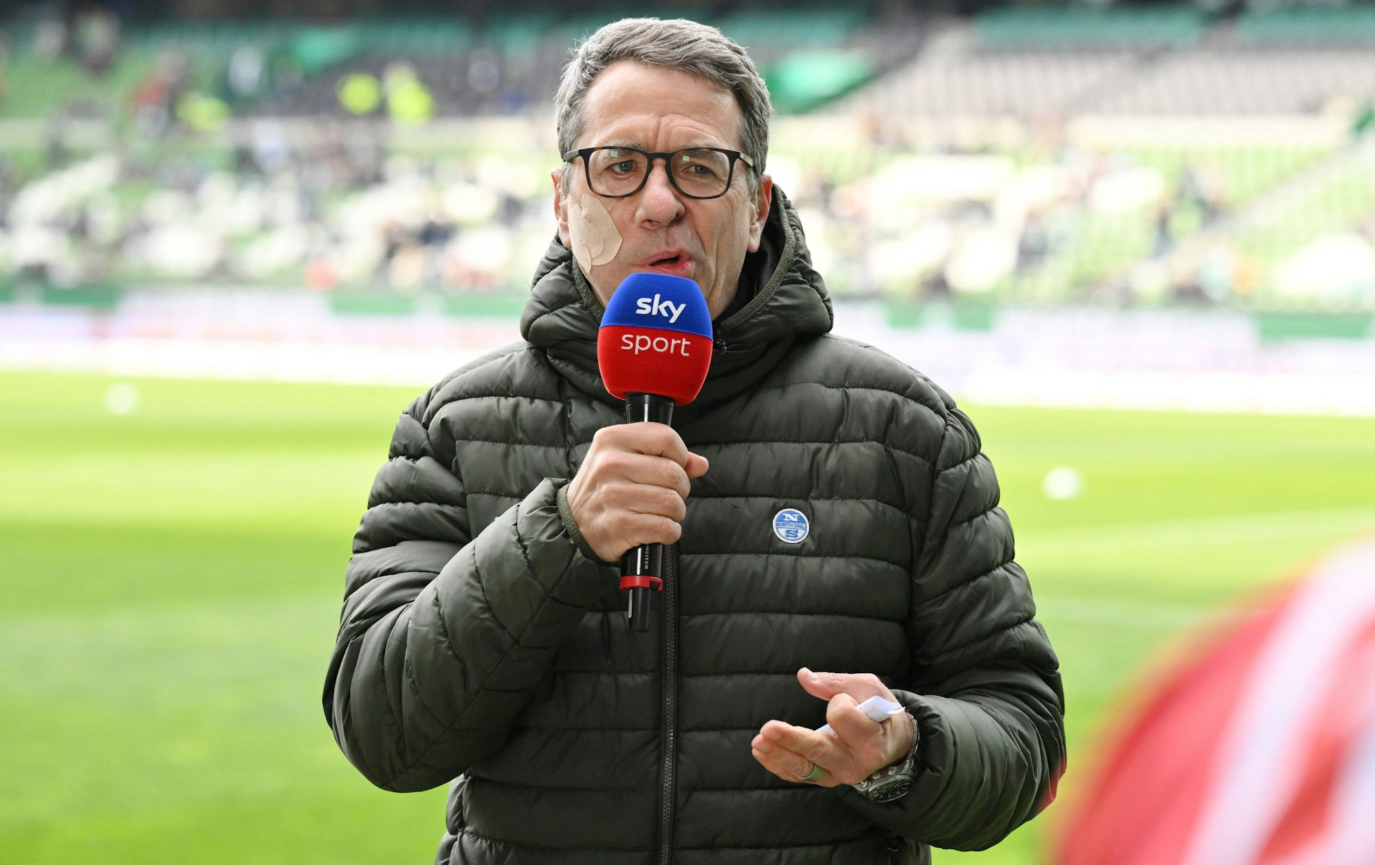 Marcus Lindemann spricht bei der Sky-Berichterstattung zur 2. Bundesliga. Er trägt wegen einer halbseitigen Gesichtslähmung ein großes Pflaster im Gesicht.