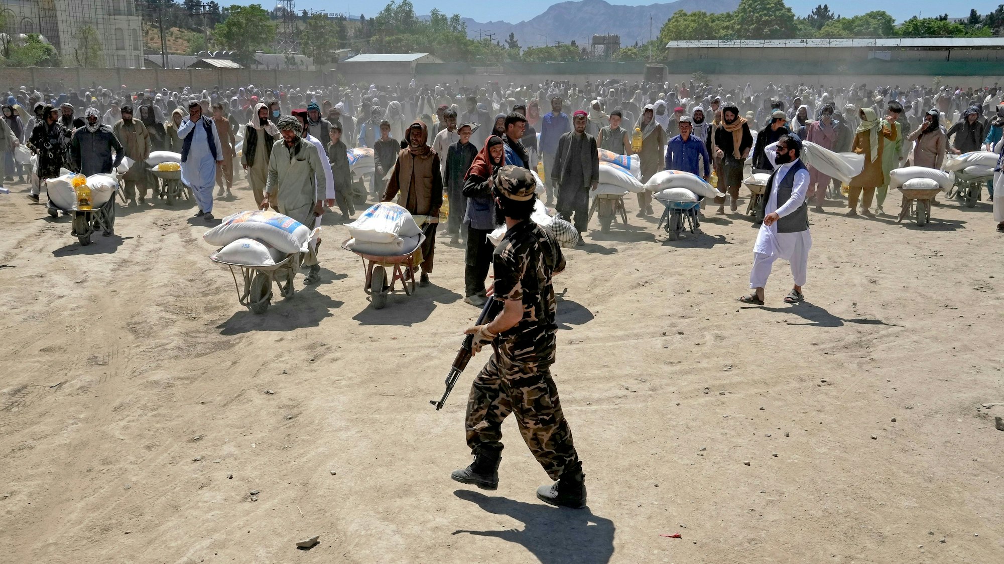 Die Taliban schreiben Frauen in Afghanistan eine Burka in der Öffentlichkeit vor. Unser Foto zeigt einen Taliban-Kämpfer, der Ende April Wache steht, während Menschen Lebensmittelrationen erhalten.