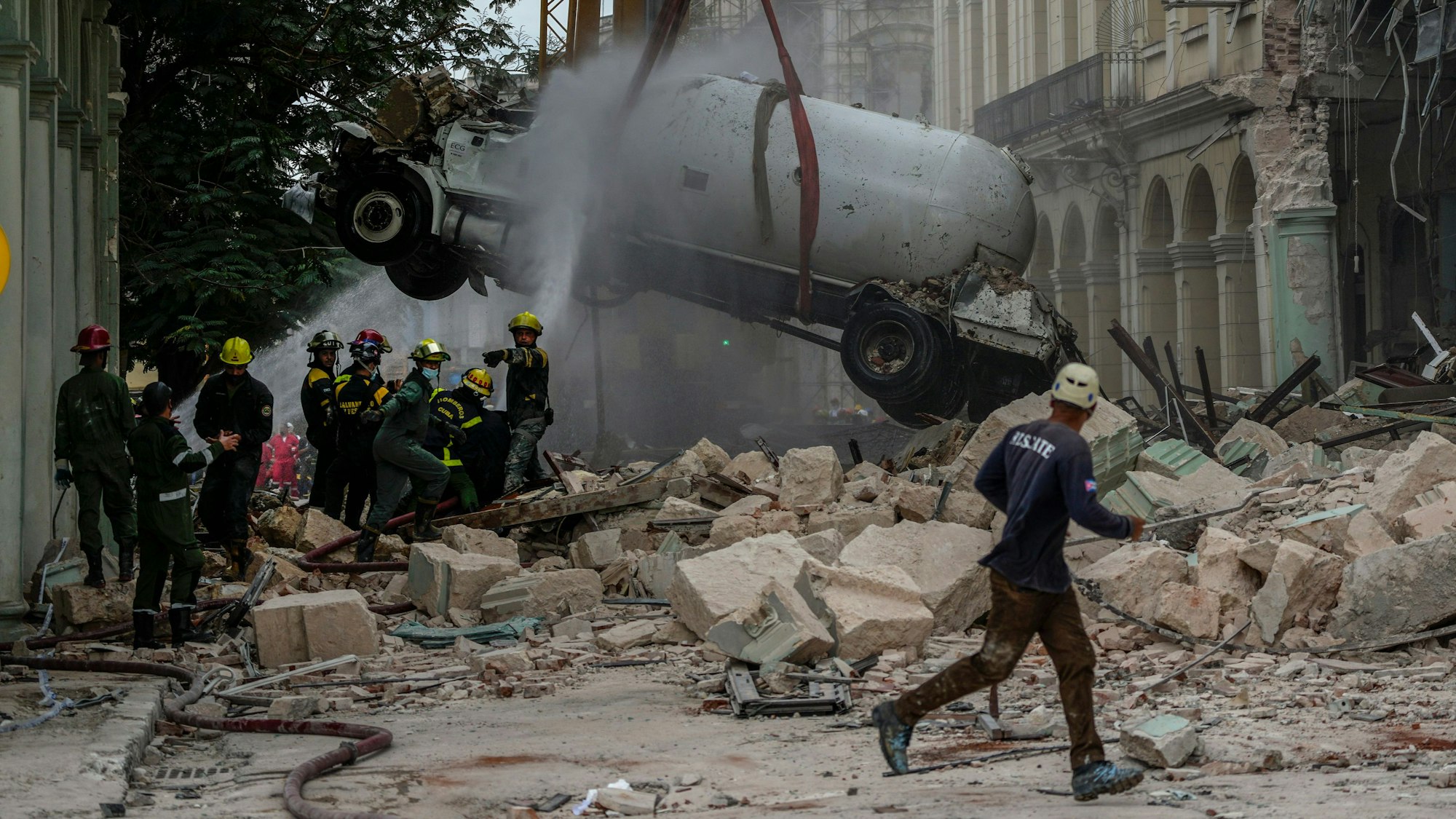 06.05.2022, Kuba, Havanna: Feuerwehrleute besprühen einen Tankwagen mit Wasser, um ihn zu kühlen, während sie ihn vom Ort einer tödlichen Explosion entfernen, die das Fünf-Sterne-Hotel Saratoga in Havanna, Kuba, zerstört hat.