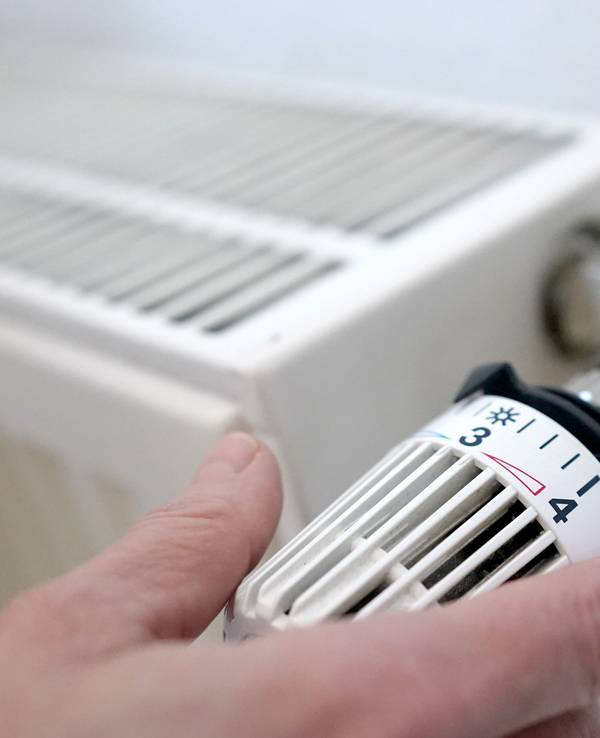 Eine Frau dreht an einem Heizungsthermostat.