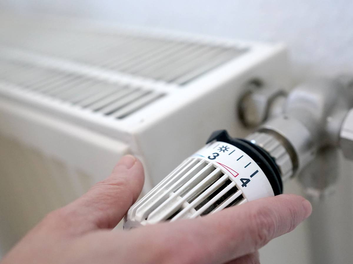 Eine Frau dreht an einem Heizungsthermostat.
