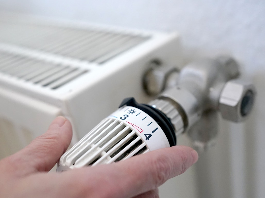 Eine Frau dreht an einem Heizungsthermostat.