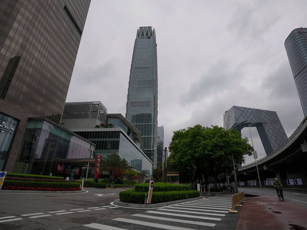 Ein Mann, der zum Schutz vor dem Coronavirus eine Gesichtsmaske trägt, fährt am 8. Mai 2022 auf einem Fahrrad an einer Straße in der Nähe des verschlossenen China World Trade Center (links) vorbei.