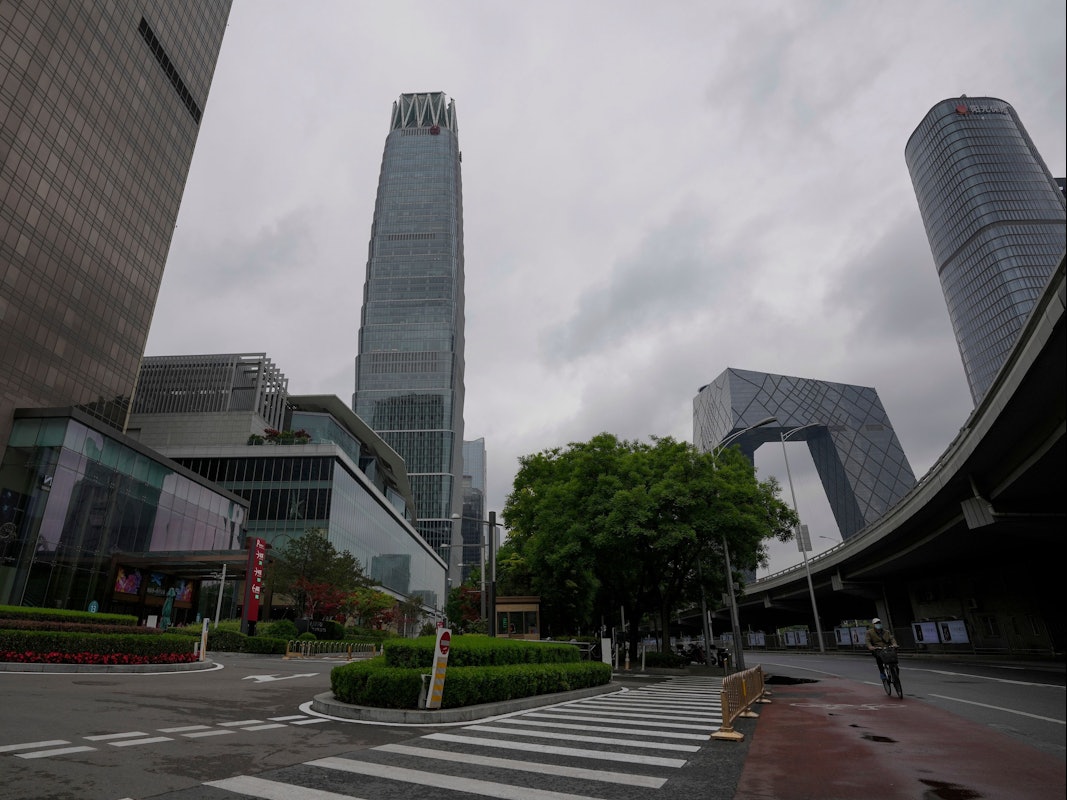 Ein Mann, der zum Schutz vor dem Coronavirus eine Gesichtsmaske trägt, fährt am 8. Mai 2022 auf einem Fahrrad an einer Straße in der Nähe des verschlossenen China World Trade Center (links) vorbei.