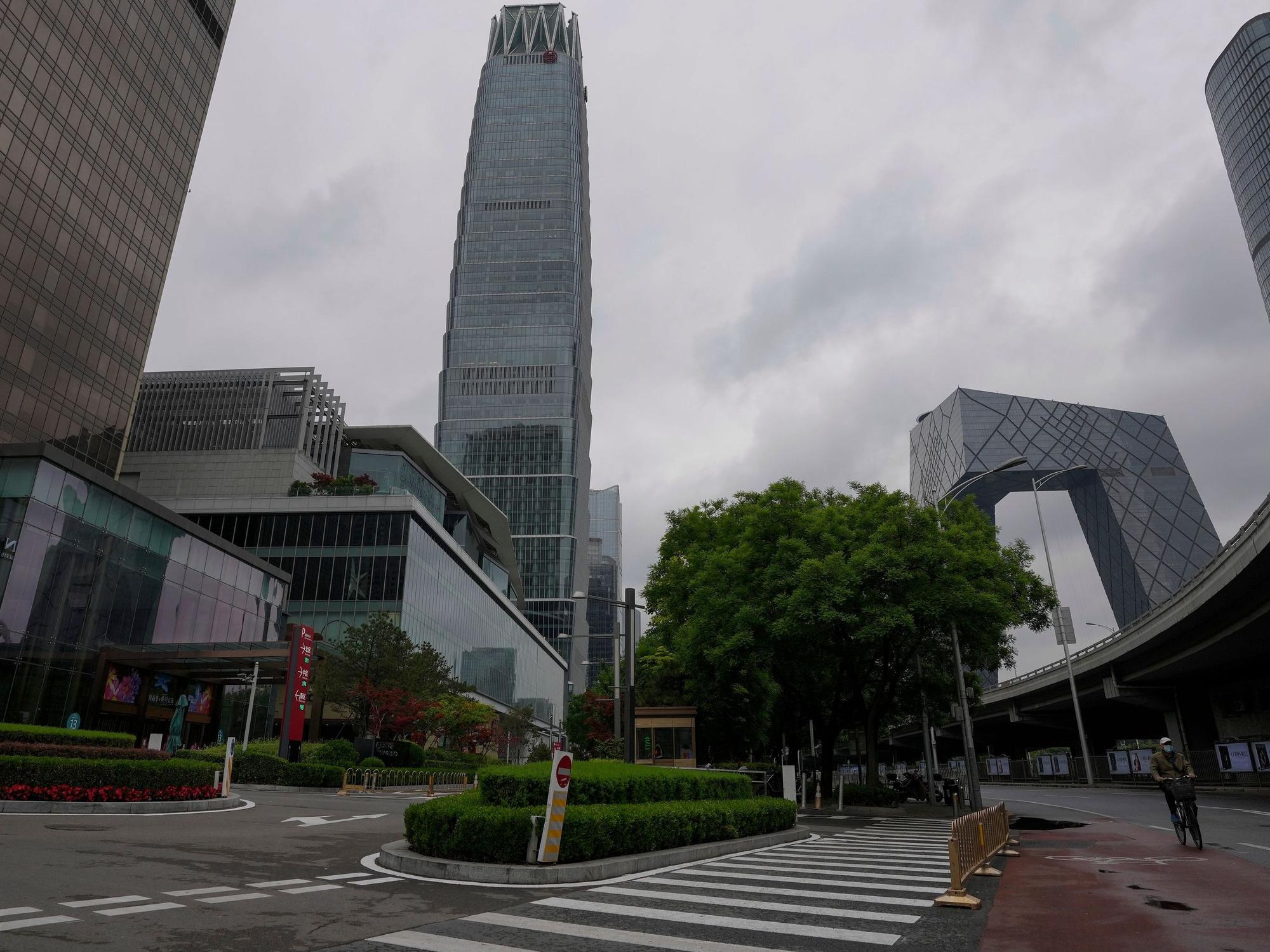 Ein Mann, der zum Schutz vor dem Coronavirus eine Gesichtsmaske trägt, fährt am 8. Mai 2022 auf einem Fahrrad an einer Straße in der Nähe des verschlossenen China World Trade Center (links) vorbei.