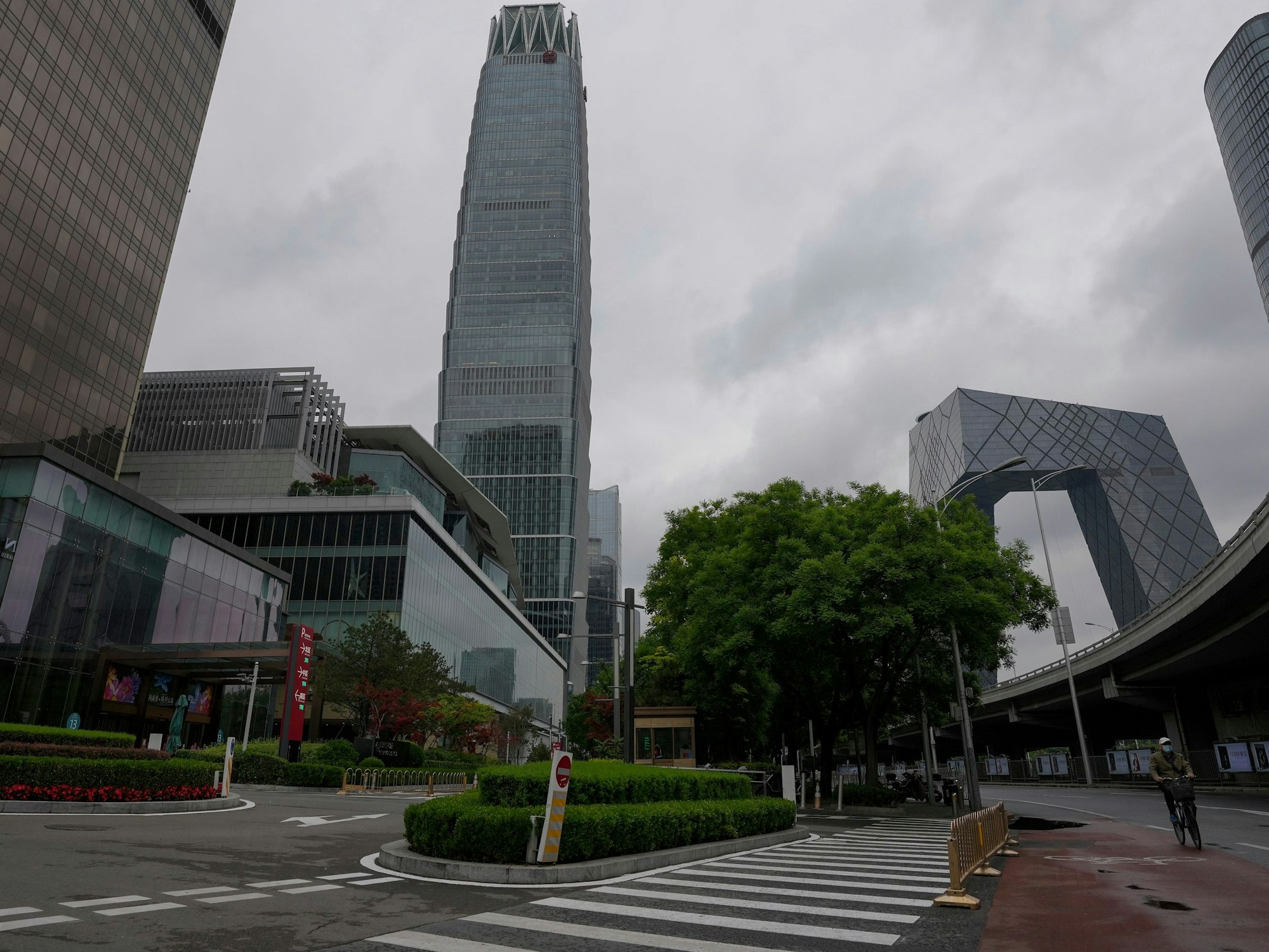Ein Mann, der zum Schutz vor dem Coronavirus eine Gesichtsmaske trägt, fährt am 8. Mai 2022 auf einem Fahrrad an einer Straße in der Nähe des verschlossenen China World Trade Center (links) vorbei.