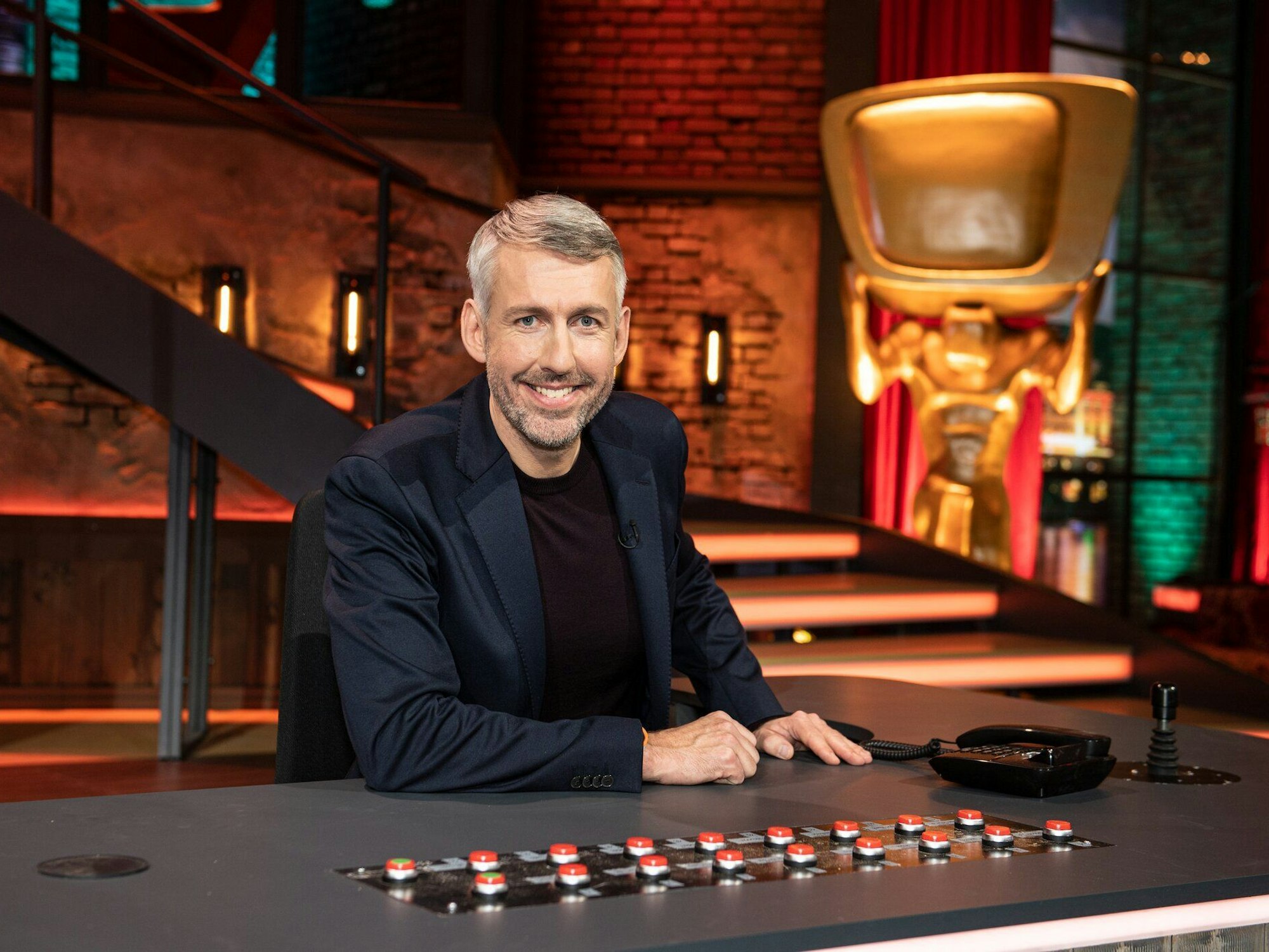 TV Total-Moderator Sebastian Pufpaff sitzt an seinem Tisch im Studio.